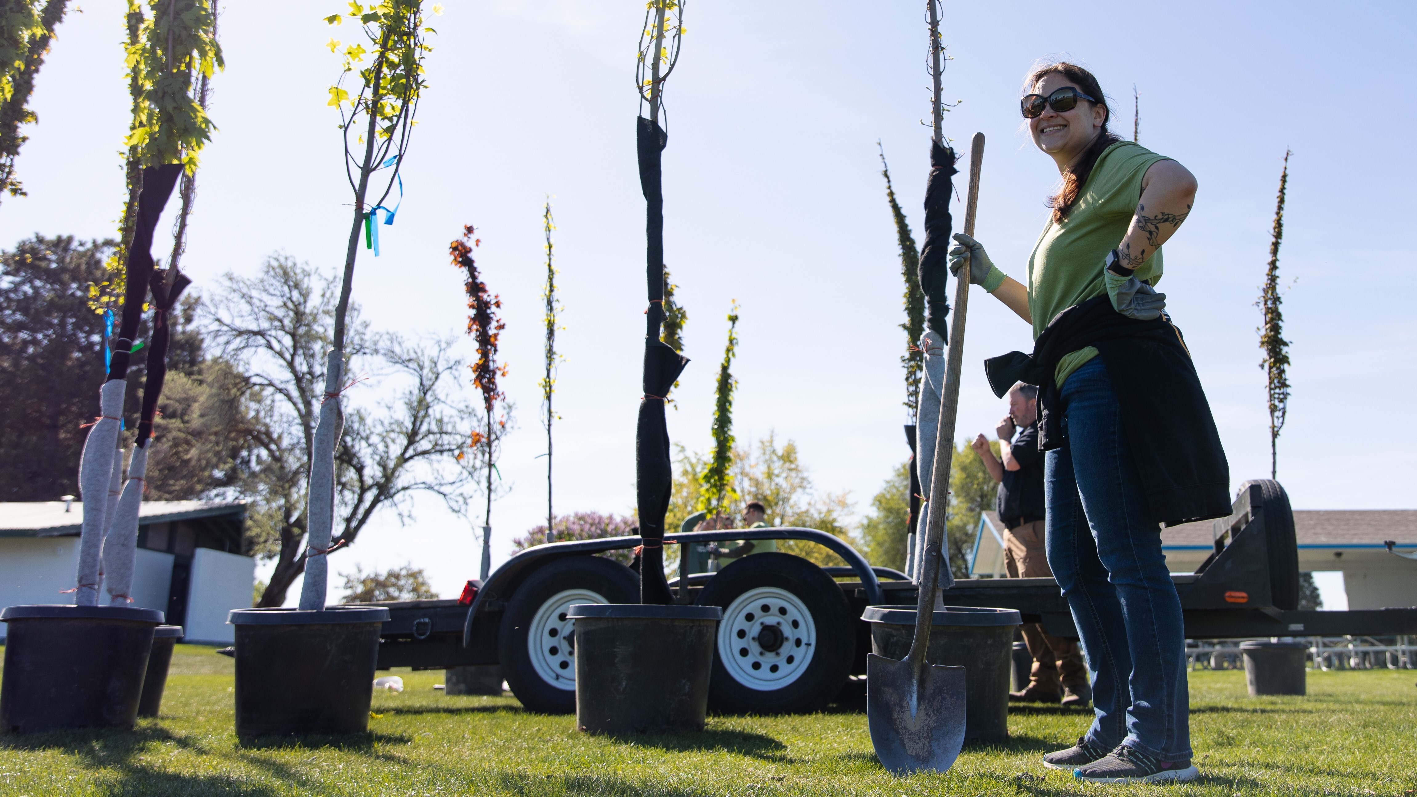 An image of a woman holding a shovel standing by potted trees.