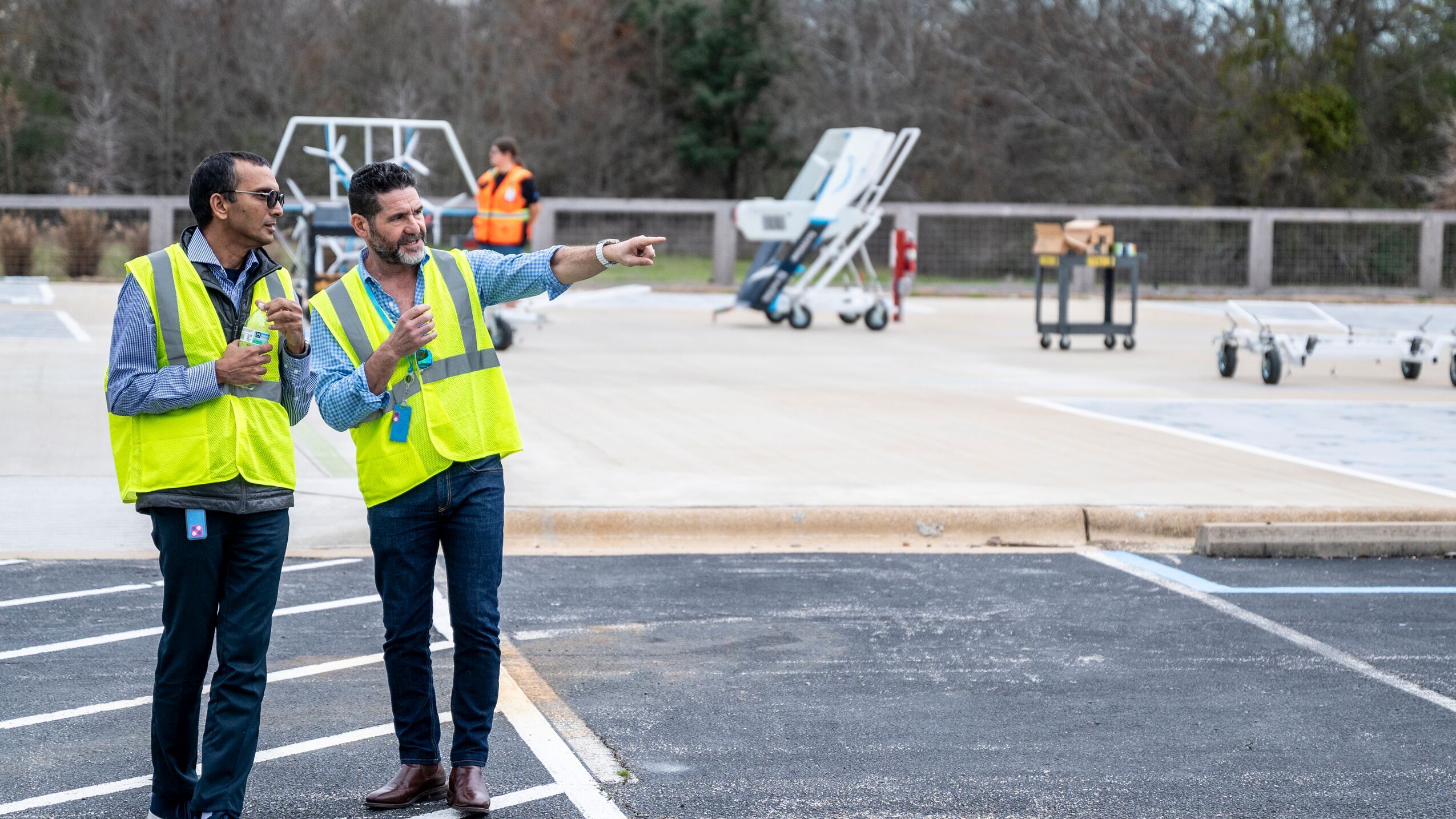 An image of Prime Air vice president, David Carbon, standing on the landing pad for Amazon's delivery drone while pointing to something in the distance and explaining something to the person next to him.