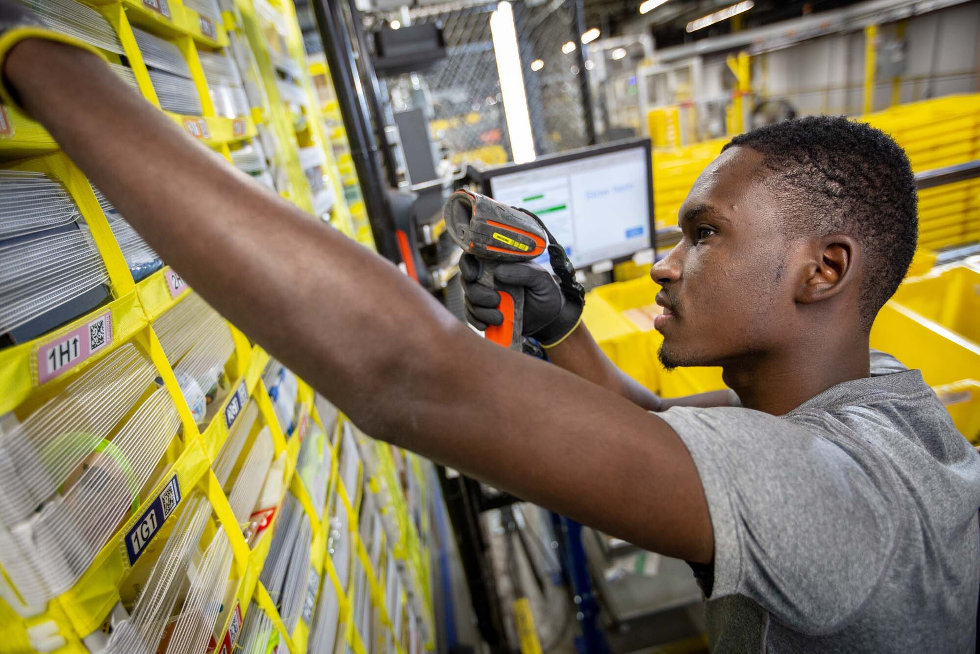 An Amazon associate holds a scanner in his left hand while reaching for a customer's product, at a Columbus, Ohio fulfillment center, CMH1