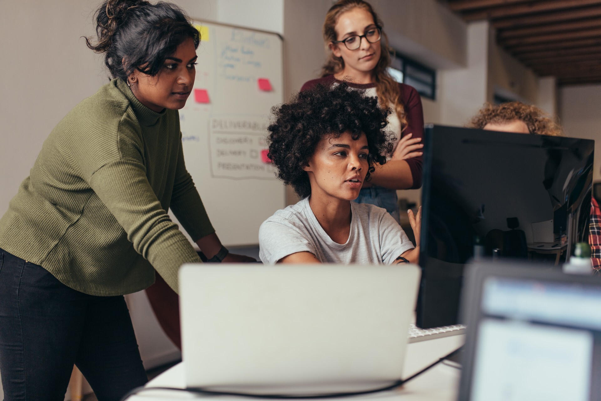 Four woman gather around a computer monitor in a classroom.