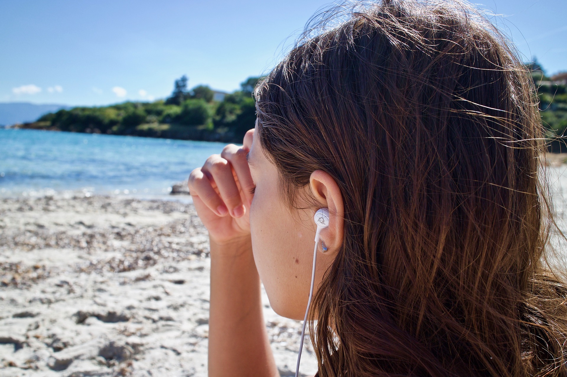 A girl listening wearing headphones and sitting on a beach