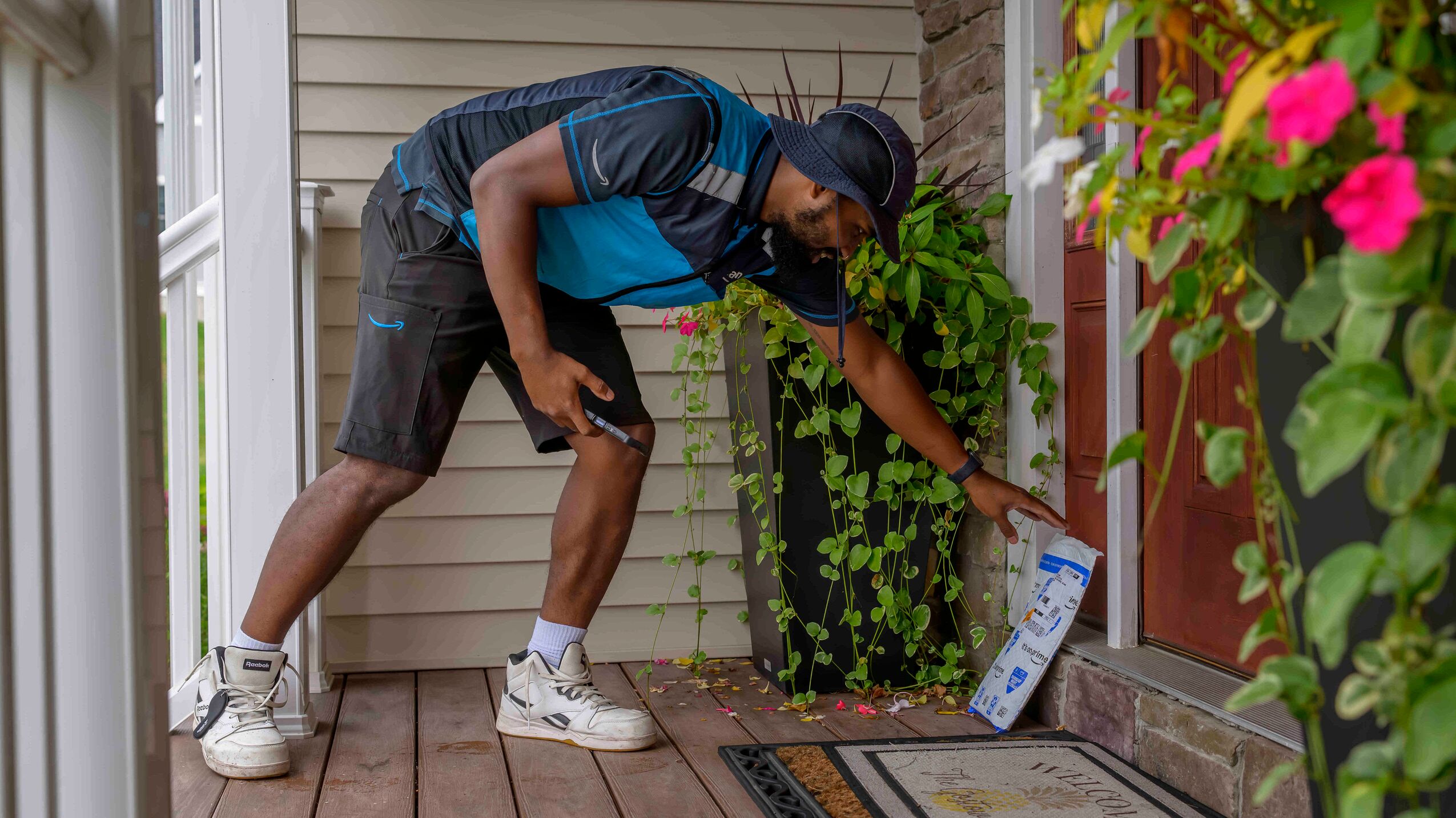 An Amazon delivery driver placing a package on a porch at the front door of a home.