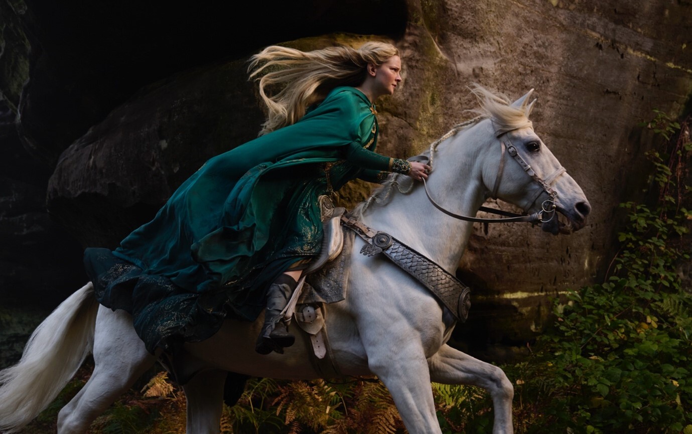 A blonde woman wearing a green cloak on a white horse