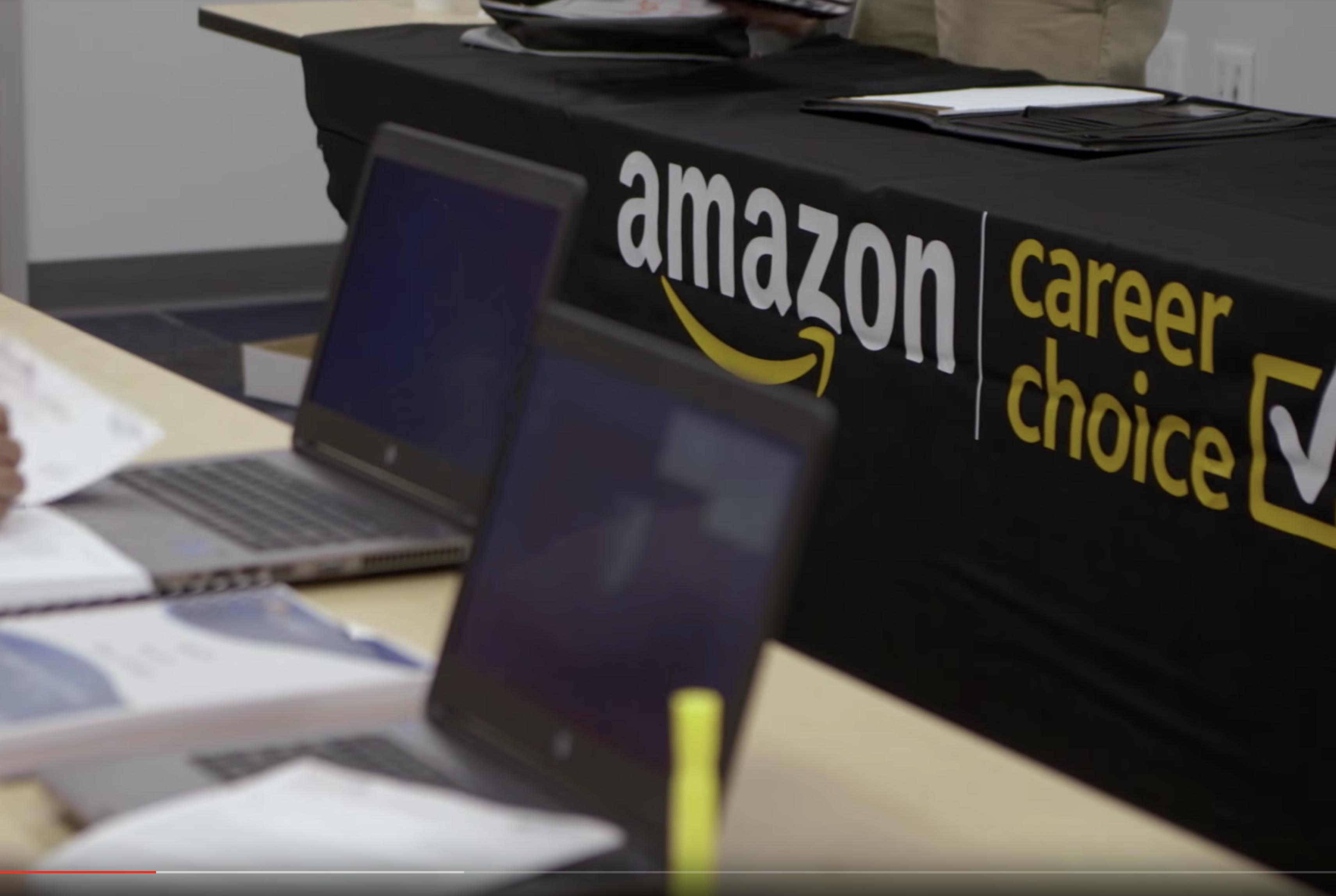 Two notebook computers sit on a table top, in front of them in a table with a drape that says "Amazon Career Choice"