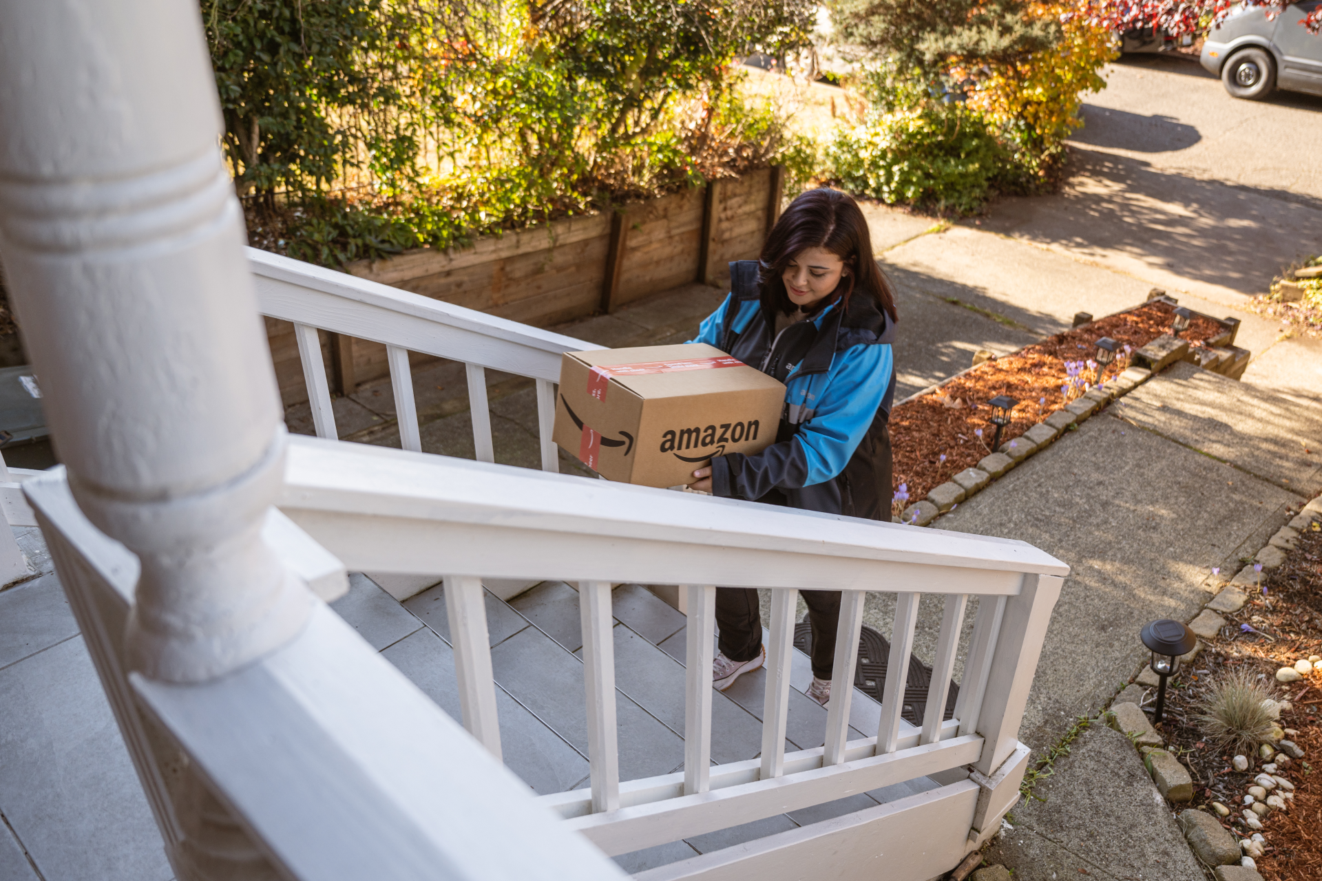 An Amazon delivery driver walks a package up the stairs to a customer's front door.