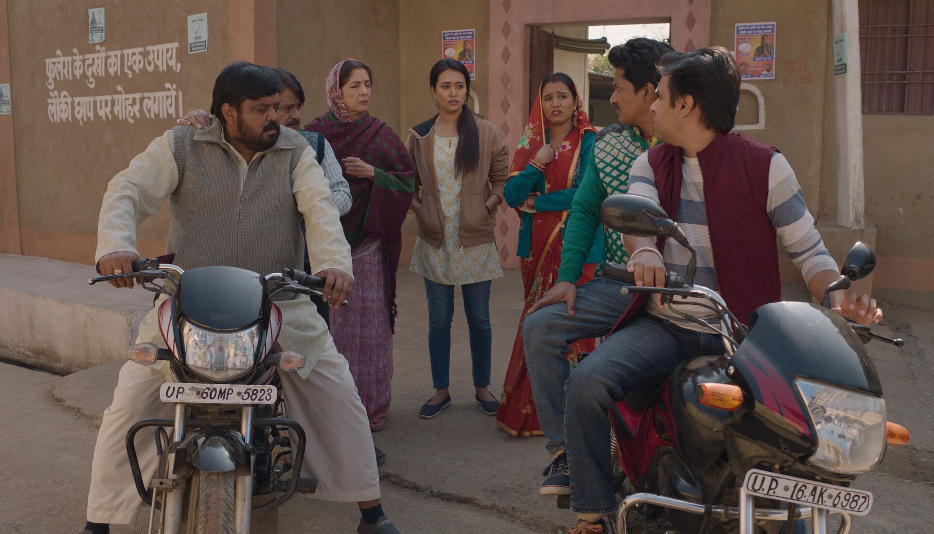 Community gathering on street corner with motorcycles in foreground