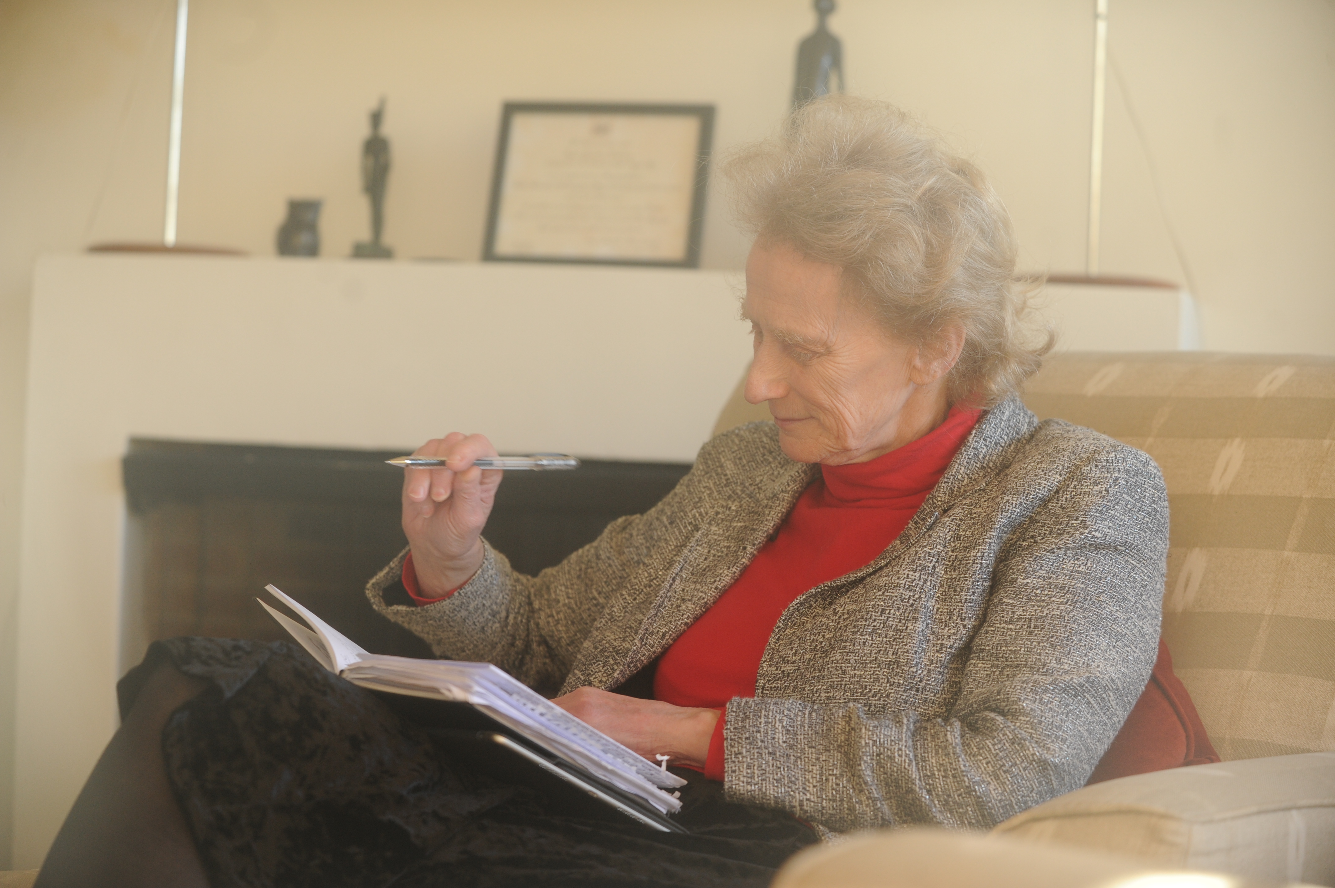 Dame Athene Donald is pictured sat on a sofa, holding a pen while looking into a notebook