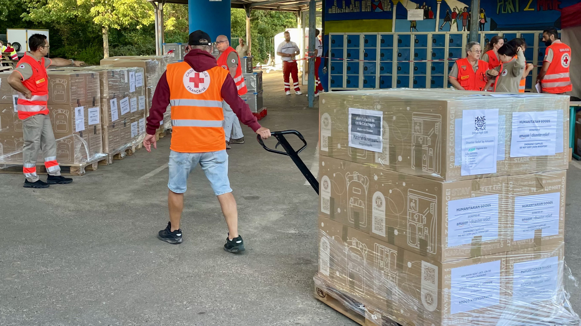 Red Cross volunteers moving pallets of humanitarian aid supplies in a warehouse