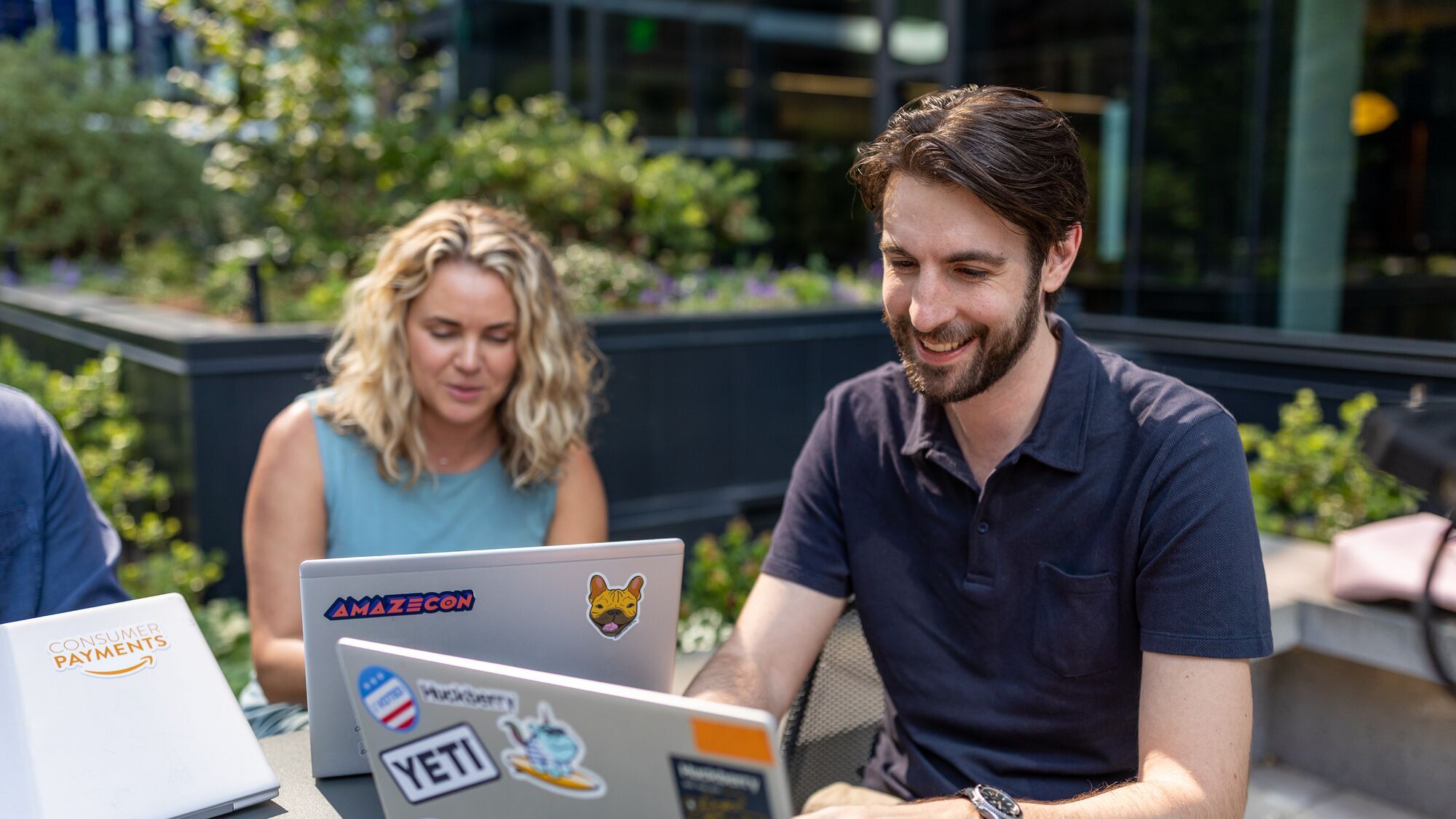 Amazon employees sit ouside at a table working on their laptops.