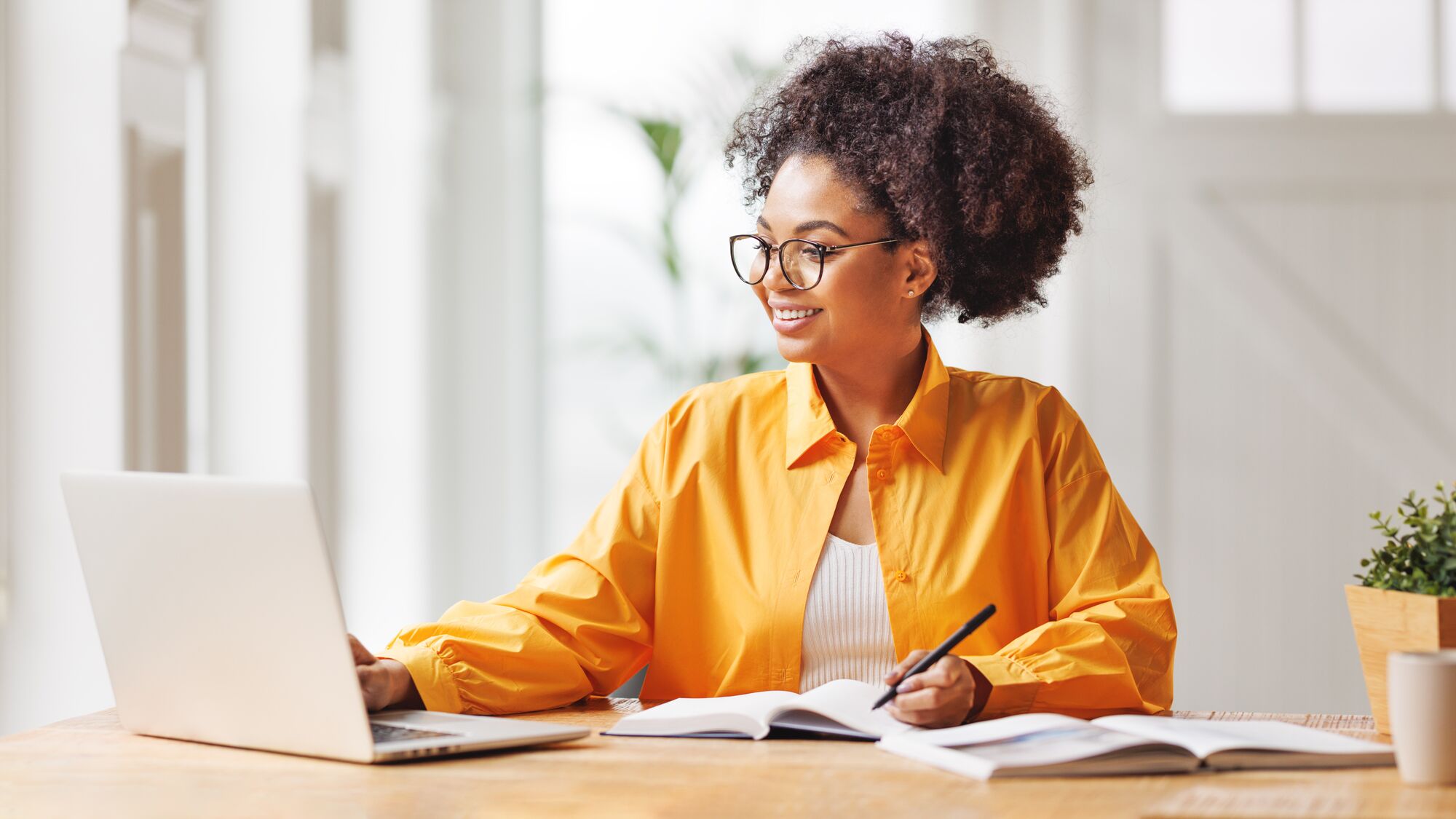 woman with glasses smiling while working on her laptop