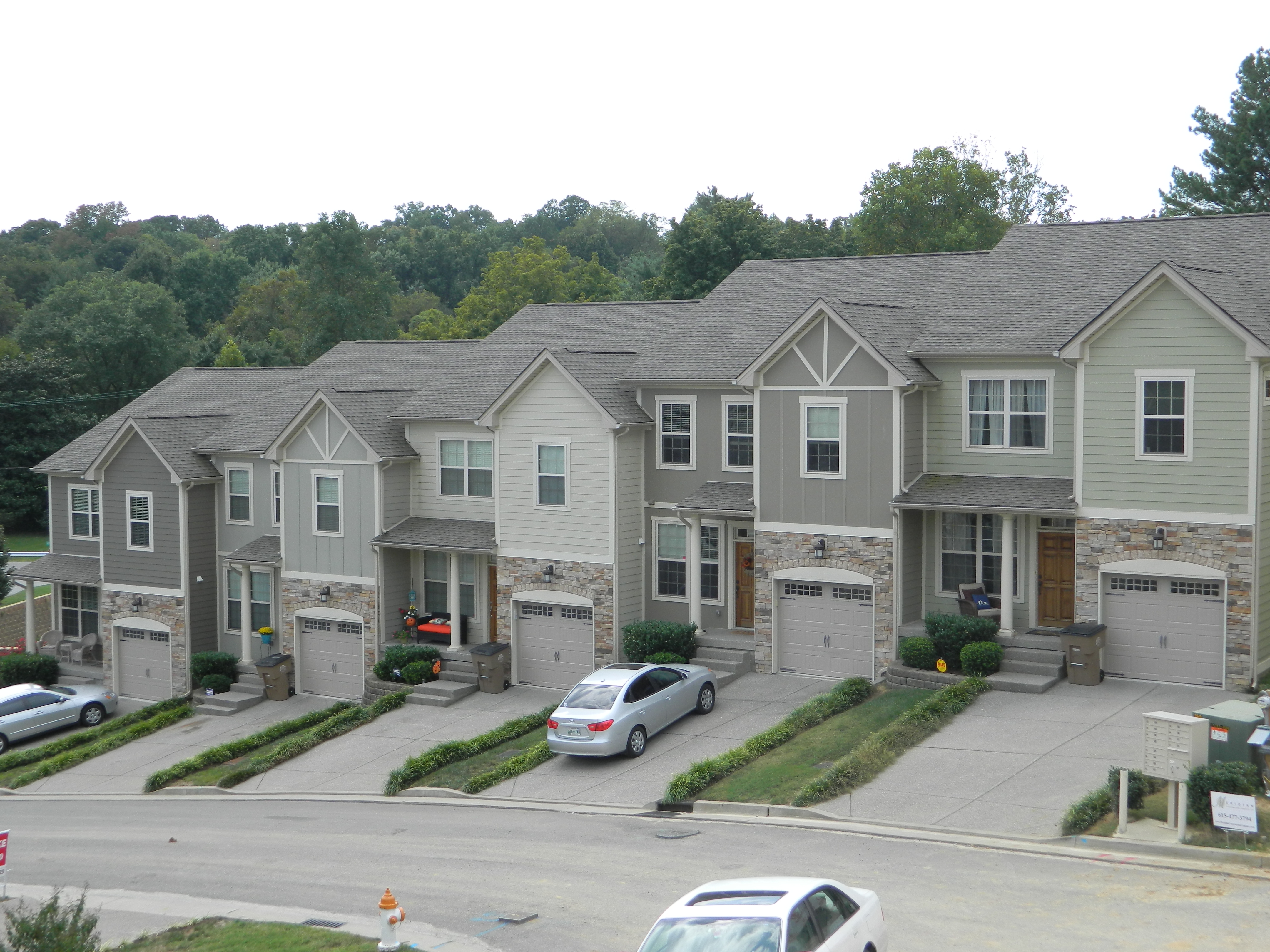 A block of connected townhouses in a neighborhood setting. Some have vehicles in their driveway. 