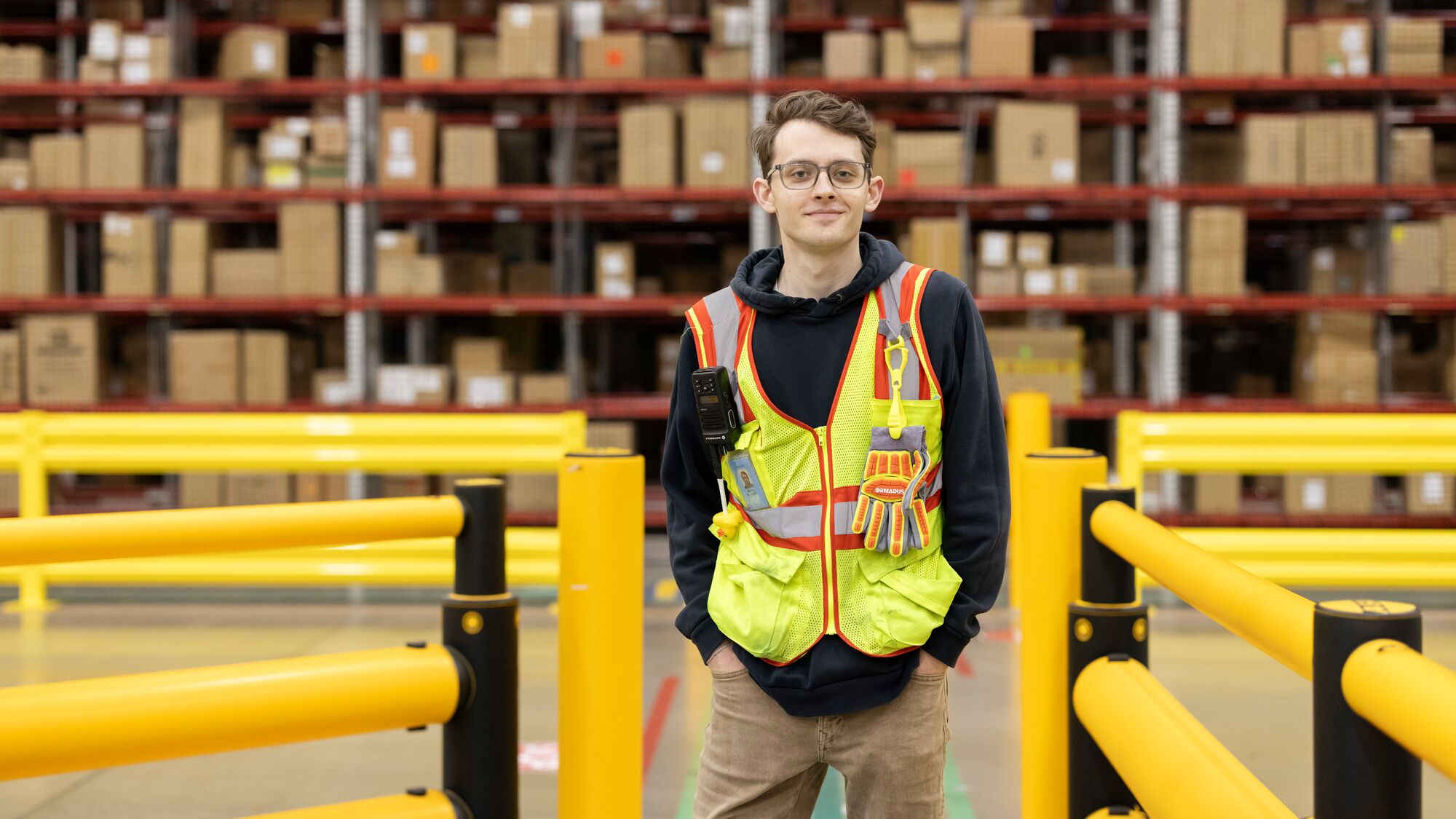 Young man in protective gear posing in front of warehouse shelving.
