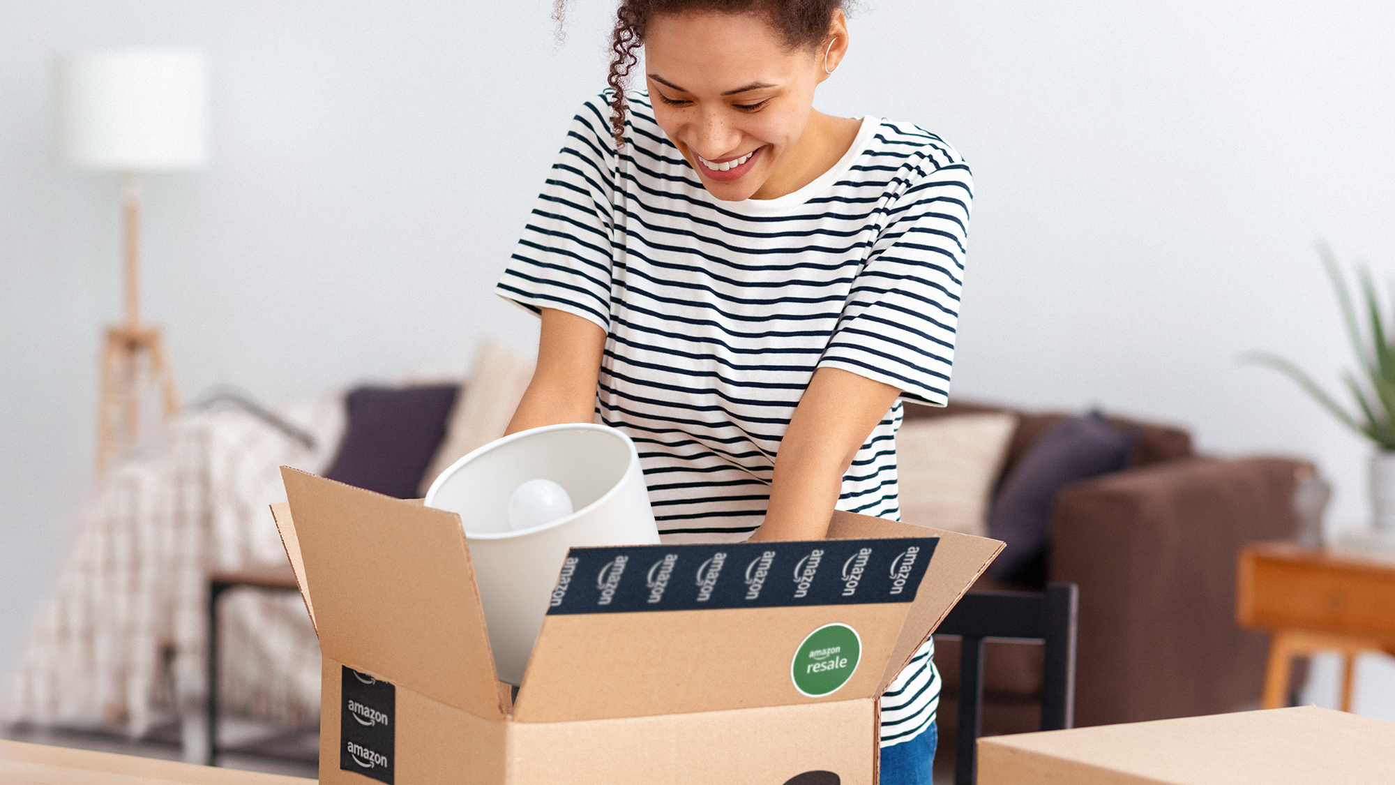 Frau lächelt beim Auspacken eines Amazon-Pakets im Wohnzimmer