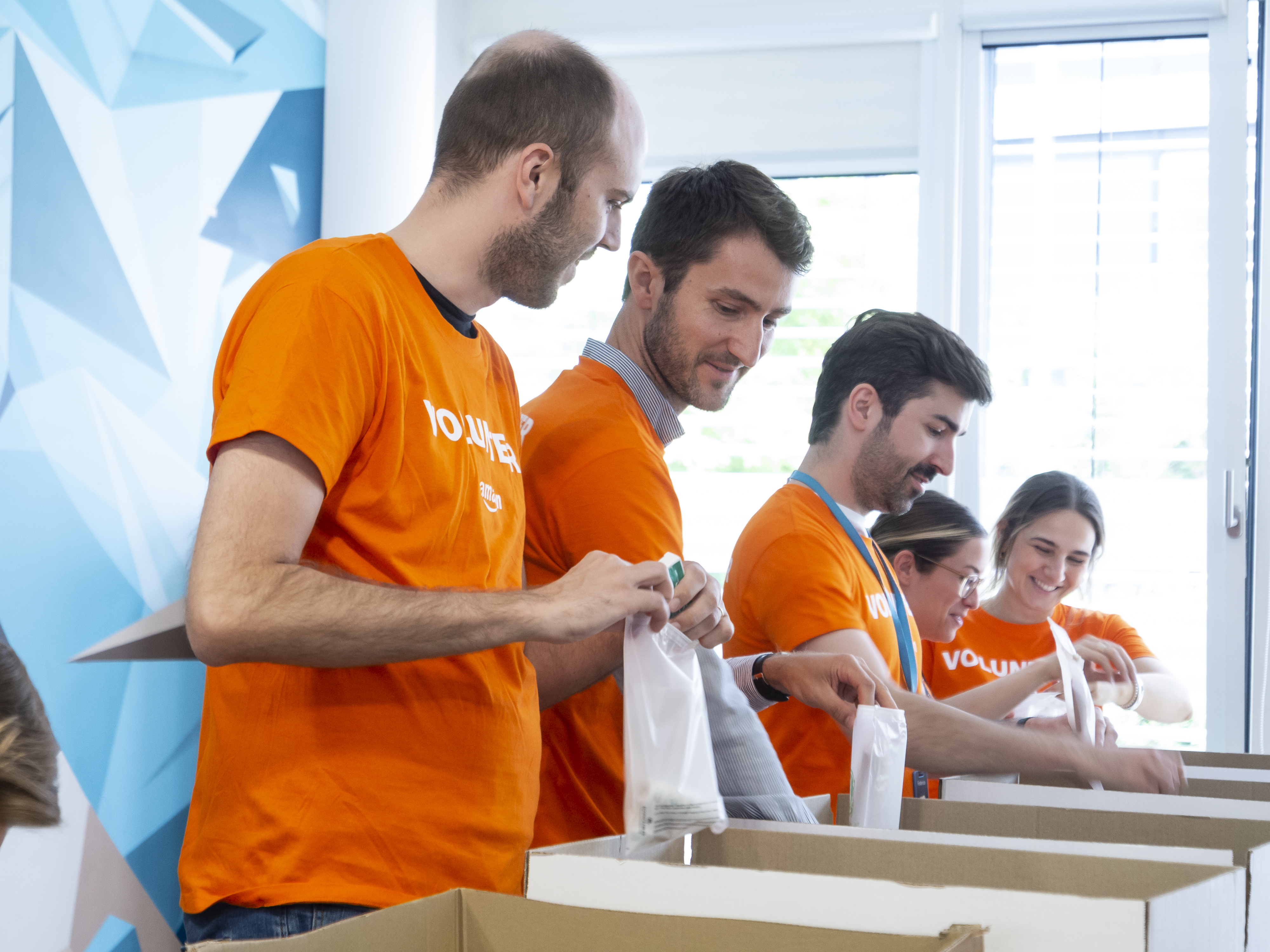 Fünf Amazonians in orangefarbenen T-Shirts beim Packen von Hygienekits für Geflüchtete