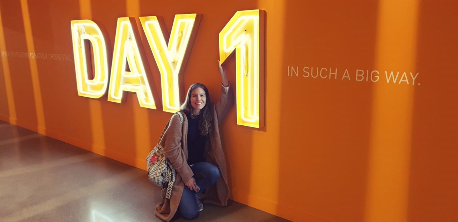 Eine Gewinnerin der Unternehmerinnen der Zukunft-Reise nach Seattle, sitzt vor einer orangenen Wand mit einer großen Leutschrift: Day 1