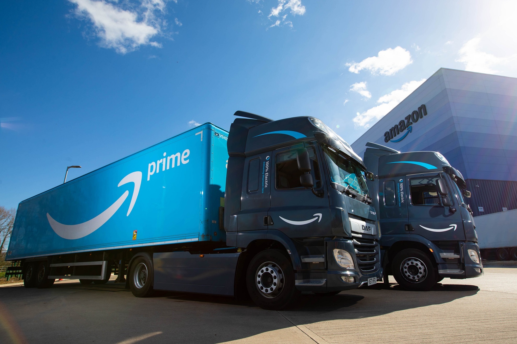 Elektrische Lkw vor einem Amazon Fulfillment Center tragen zur Elektrifizierung des Transportnetzwerks bei.