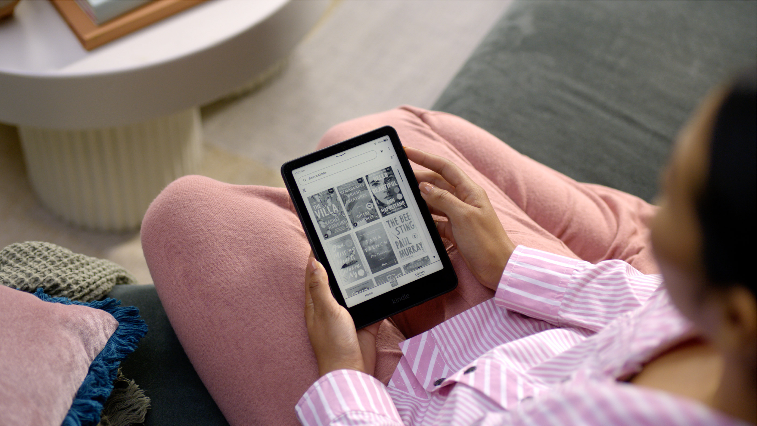 Woman on a sofa holding a Kindle showing a selection of book covers