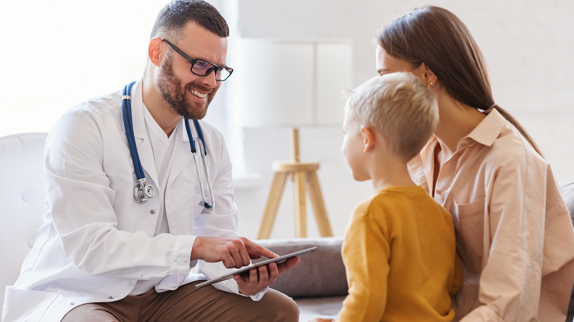 A doctor pointing at a tablet device and talking with a mother and her child.