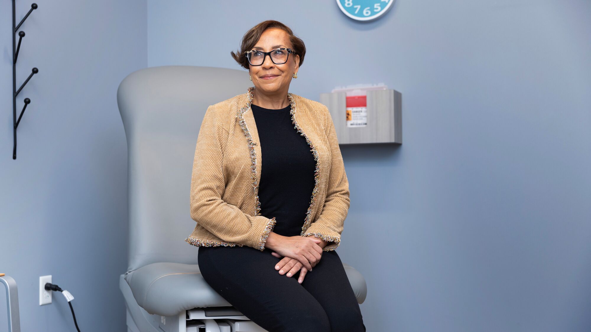 Woman in medical exam room wearing tan cardigan and glasses