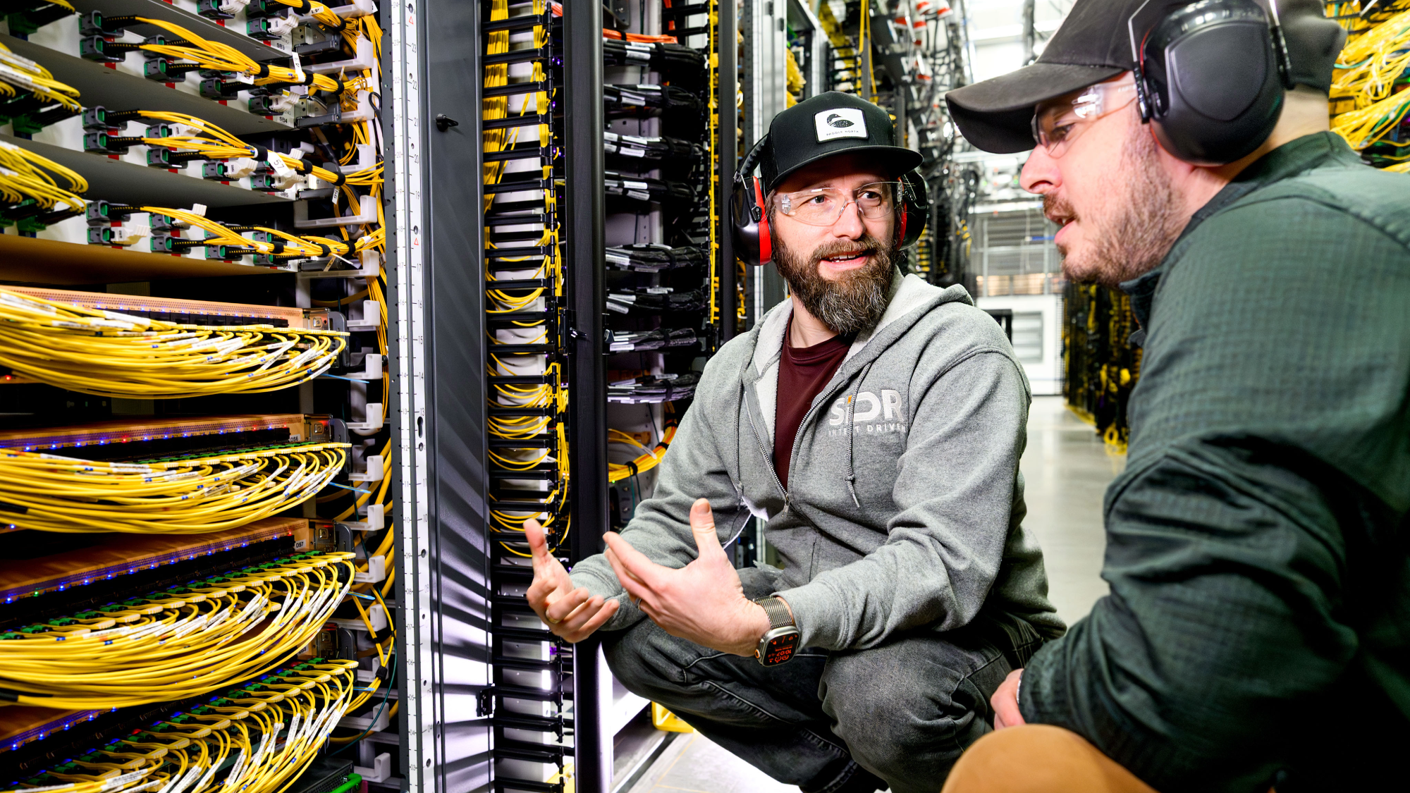Amazon employees wear safety gear and work in a data center.