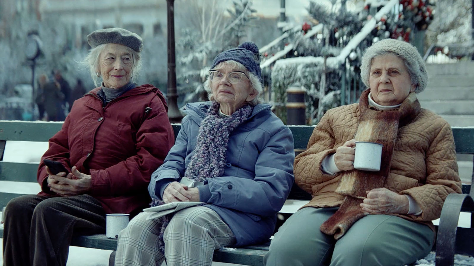 Die drei Freundinnen im Amazon Weihnachtsspot 2023 winterlich bekleidet auf einer Parkbank.