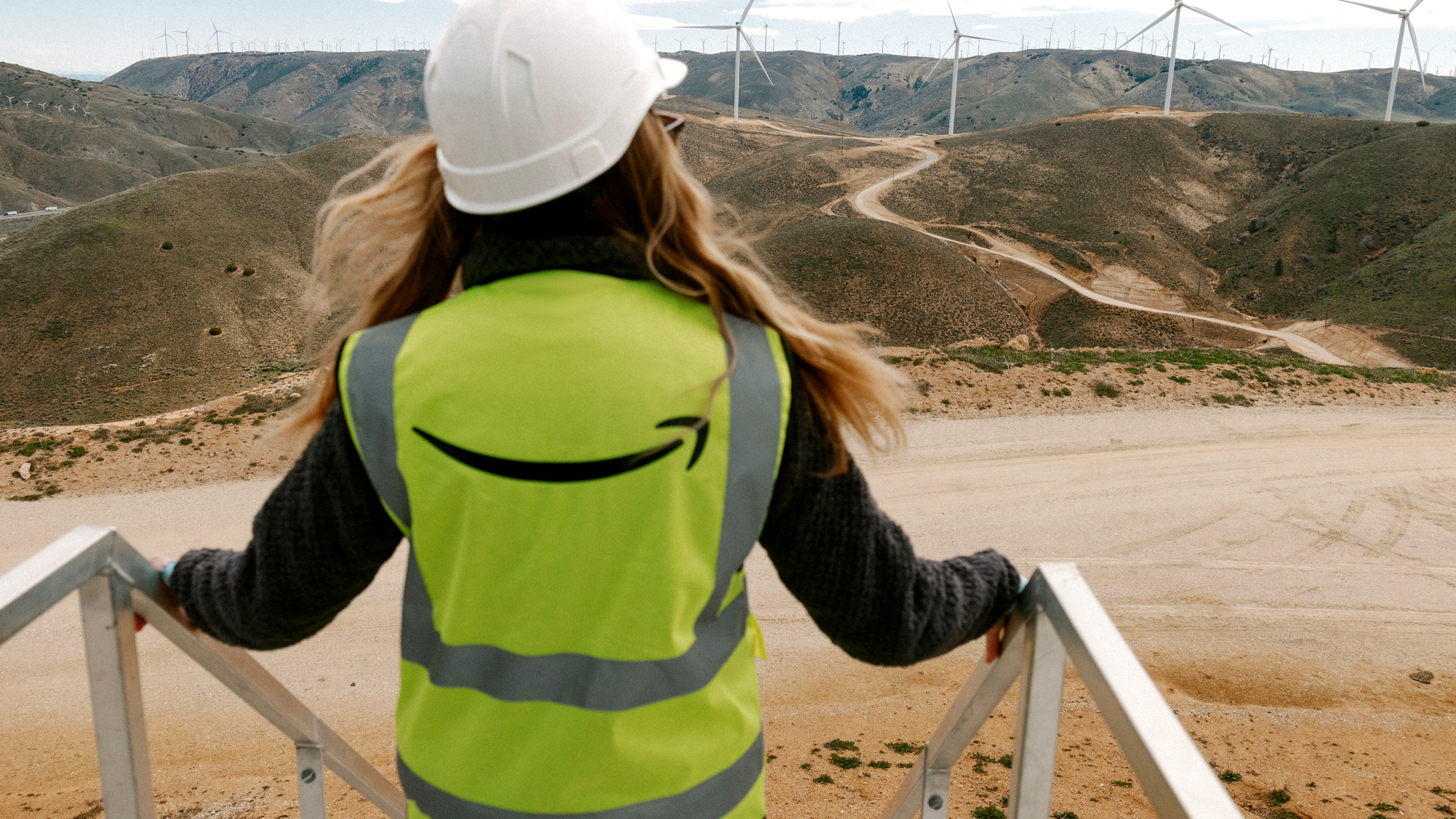 Woman in Amazon safety vest overlooking at windy landscape covering in wind turbines