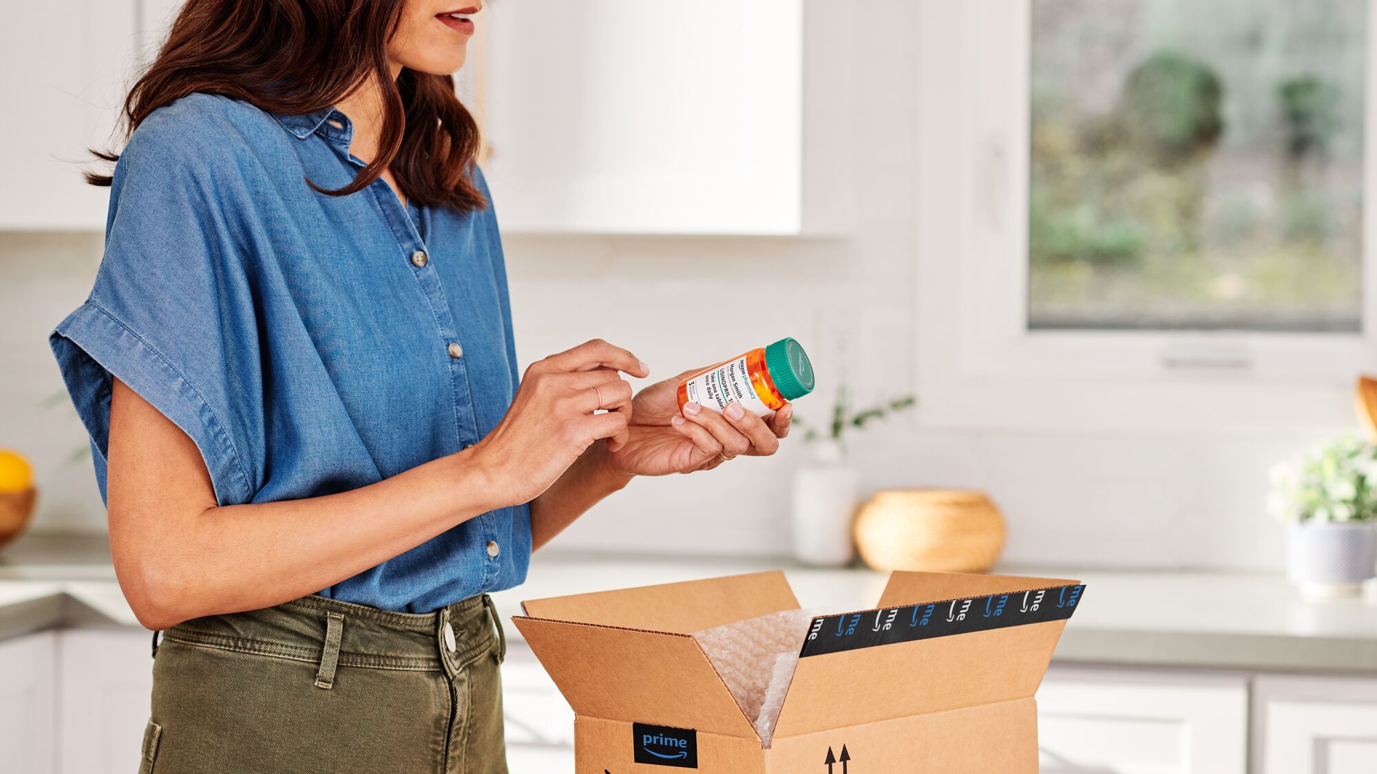 Woman in denim shirt  unpacking prescription from delivered Amazon box in kitchen