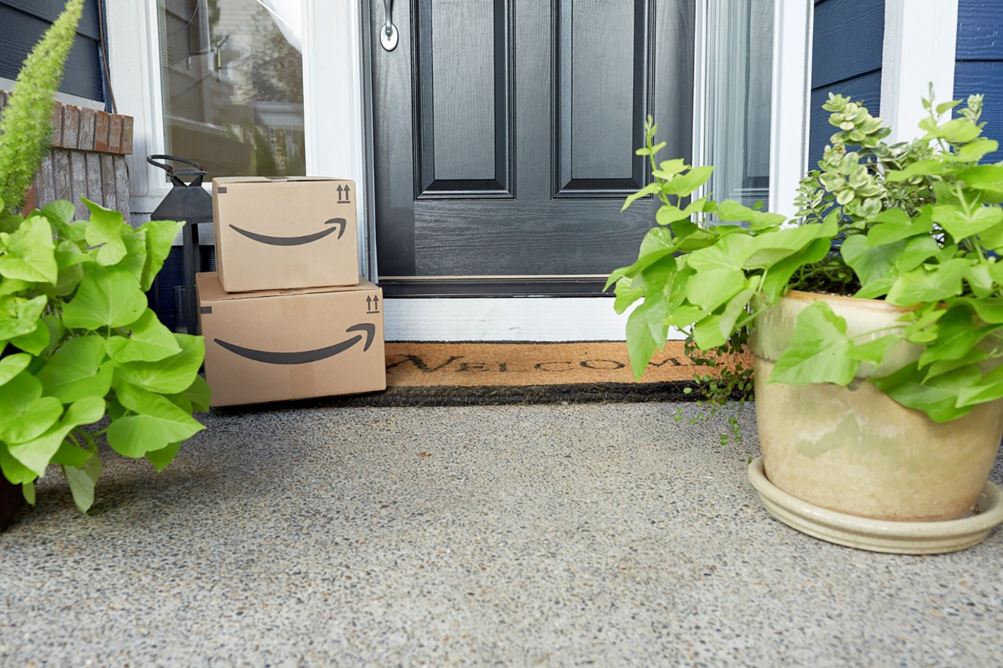 Two Amazon boxes or packages stacked on a door mat on a front step. 