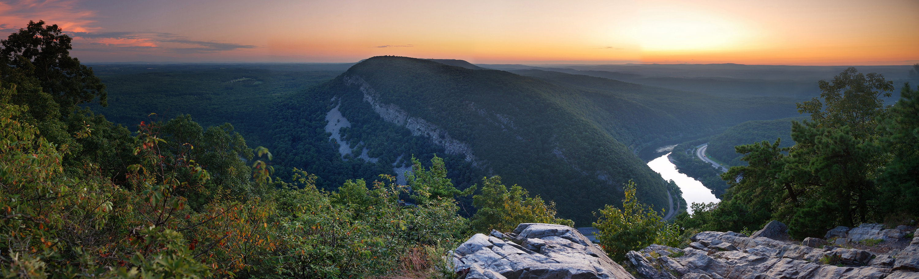 A view of the Appalacian mountains in Pennsylvania overlooking mountains, river, vegetation, in front of a sunset.