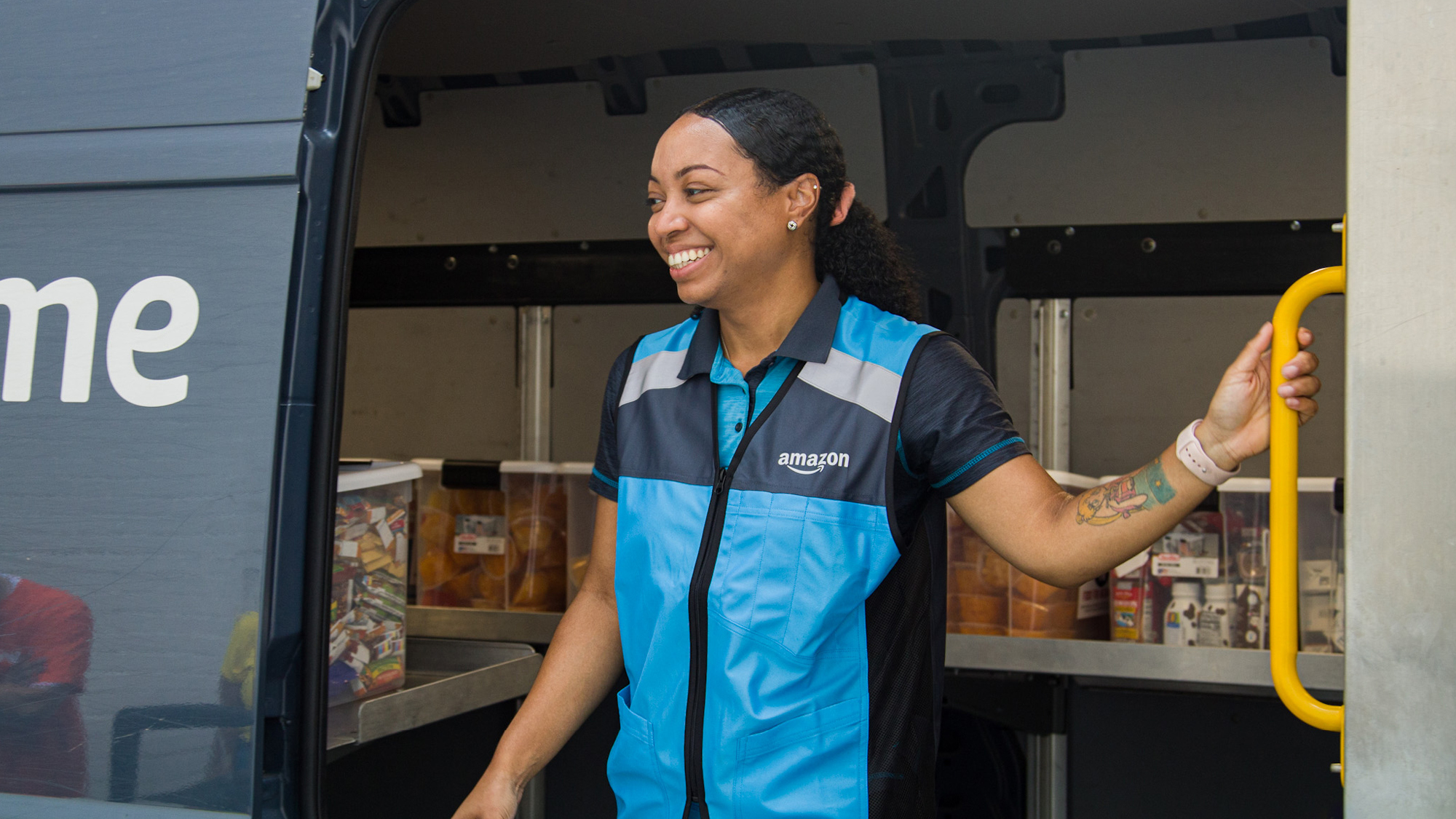 A photo of an Amazon delivery driver standing at the opening of a delivery van. There are bins inside the van that are holding donation items. 