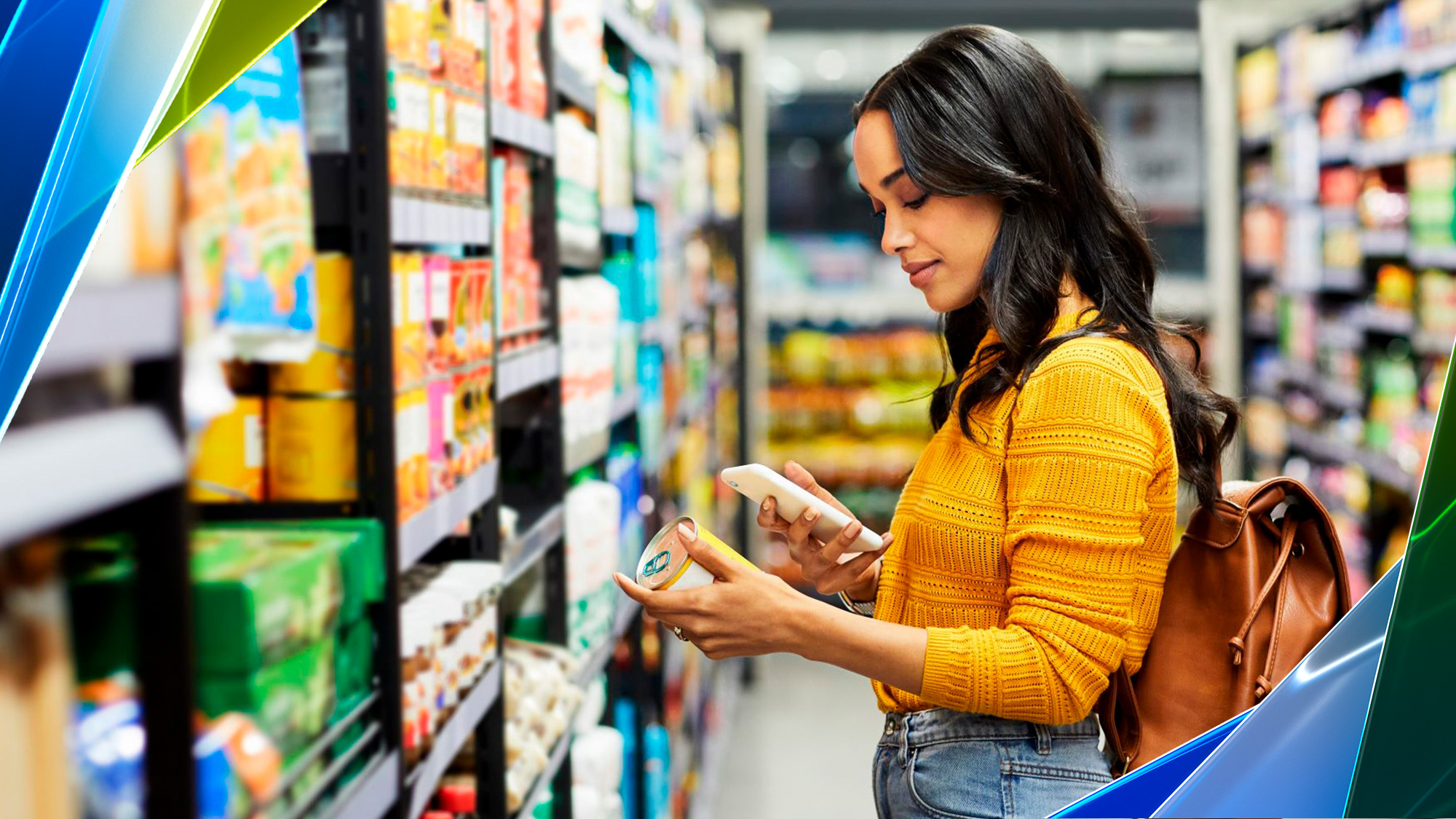 A woman stands in a grocery store aisle and holds a can of food while looking at her phone.