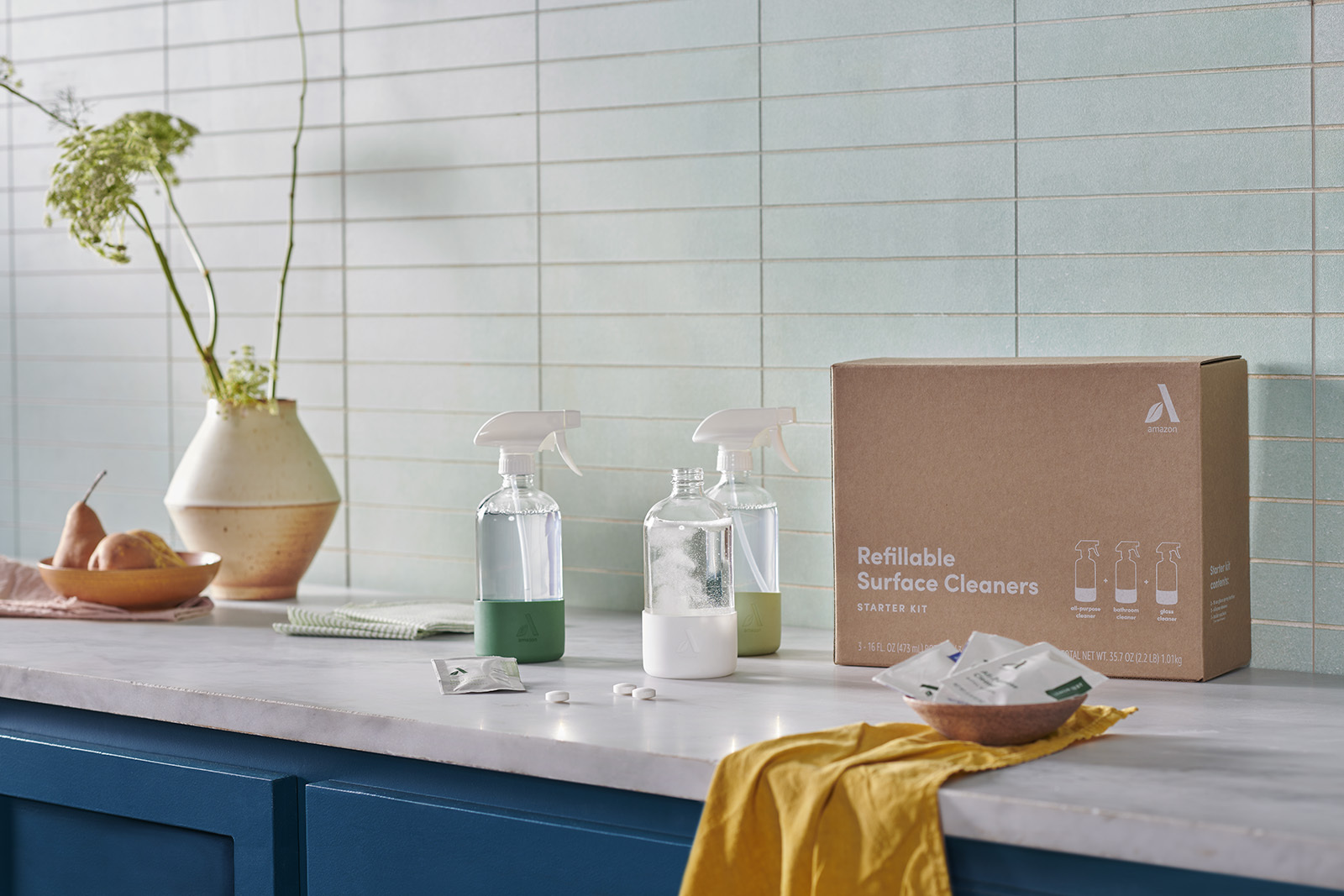 An image of cleaning products and a cleaning cloth sitting on a kitchen counter. There is a brown box beside the products that they were delivered in.