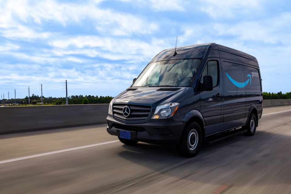 A cargo van decorated with the Amazon smile logo and the word "Prime" drives down the road.