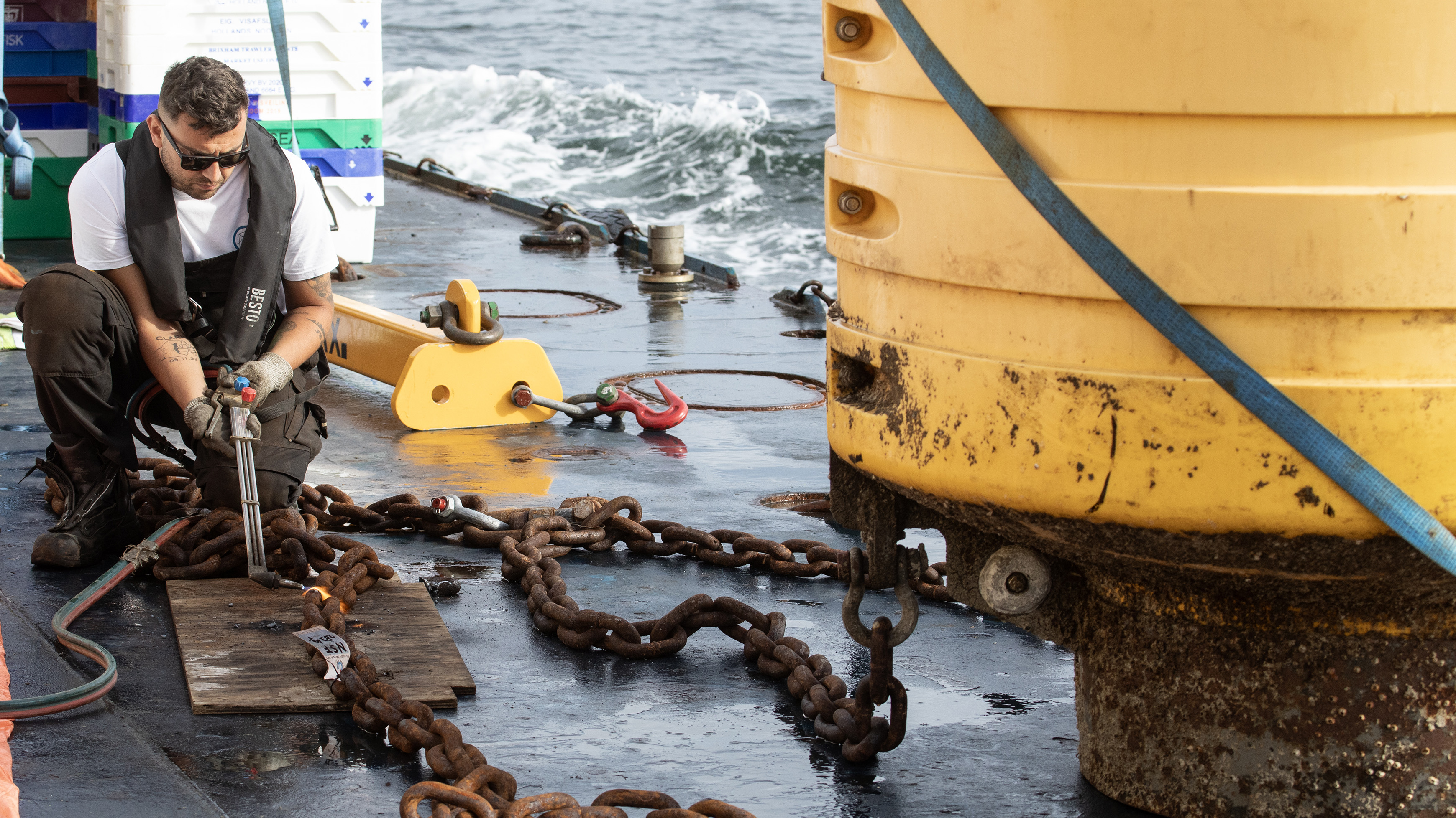 Worker repairing heavy chains on ship deck near ocean