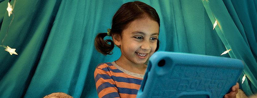Child sitting on couch outdoors using a Fire tablet