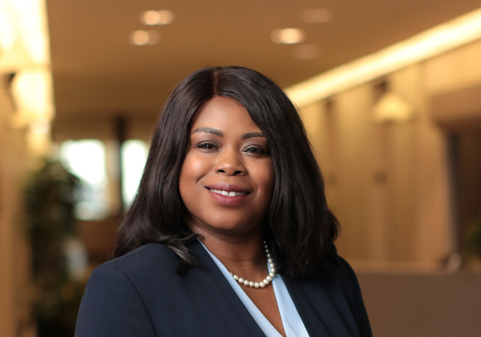 An image of a woman smiling for a professional headshot photo with a large hallway in the background. 