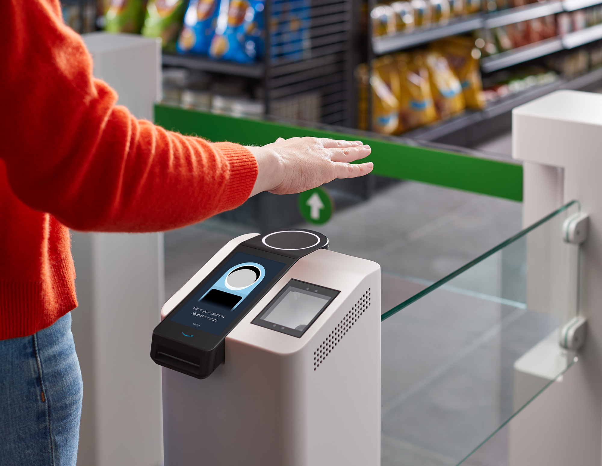 A person stands at a grocery entry gate with their hand suspended over a palm reading device. 