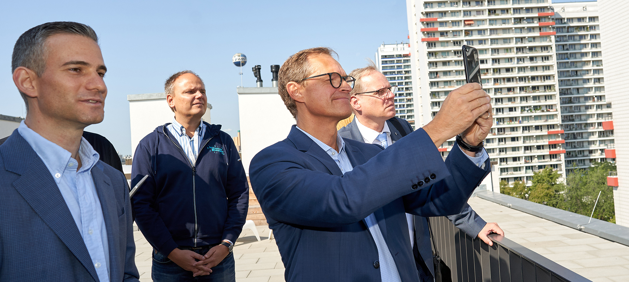 Der Bürgermeister von Berlin, Michael Müller, steht mir den Amazon Kollegen auf dem Dach den Amazon-Gebäudes. Sie genießen die Aussicht und machen Fotos der Skyline.