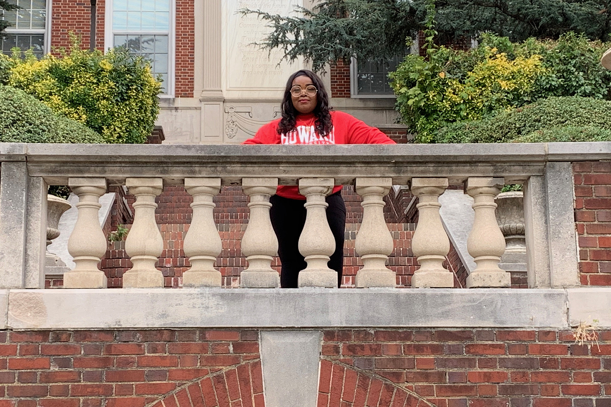 A student photographed on a college campus. She wears a red sweatshirt with the word "Howard" in white letters.