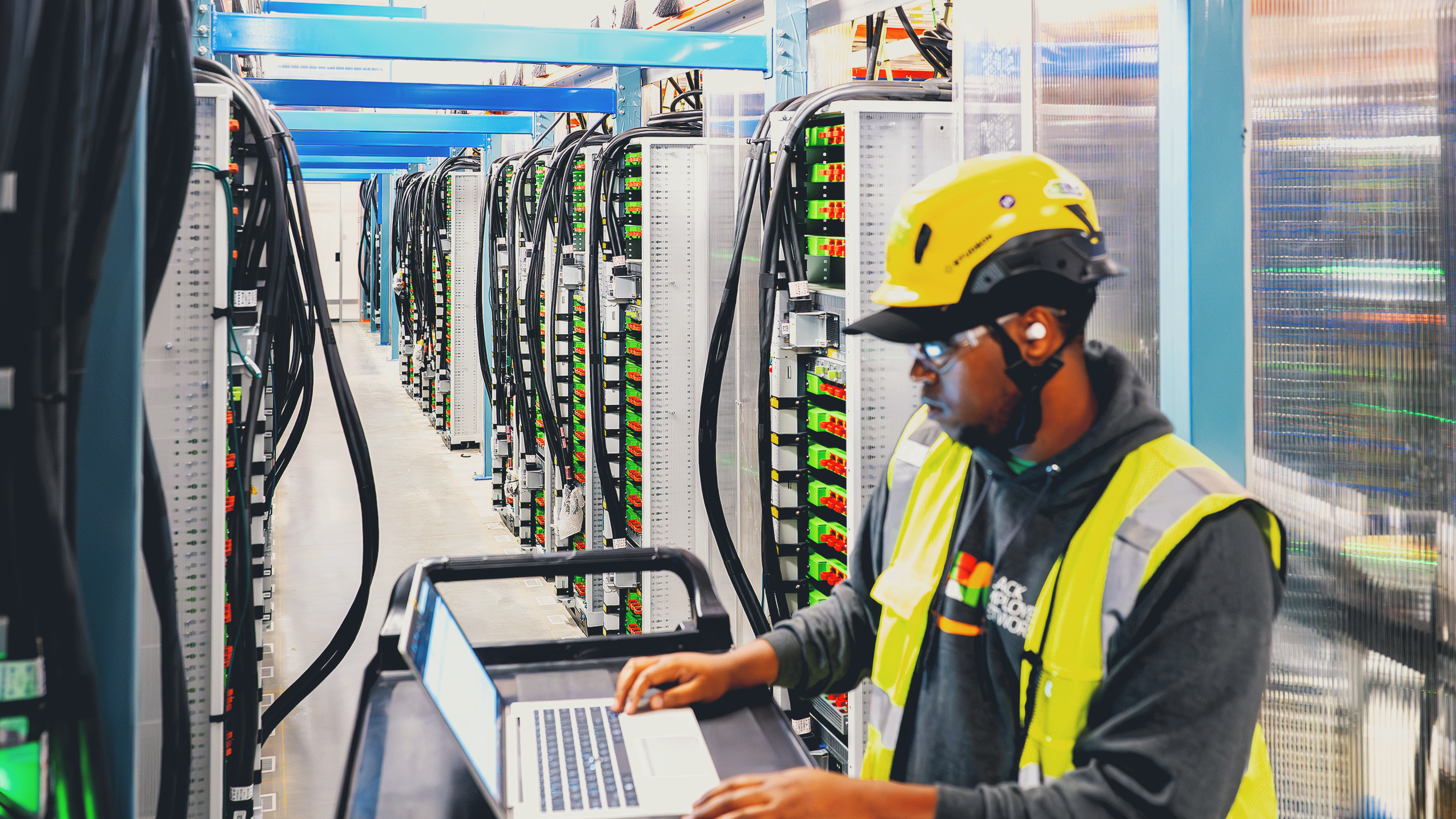Amazon employee in safety gear using laptop in server room