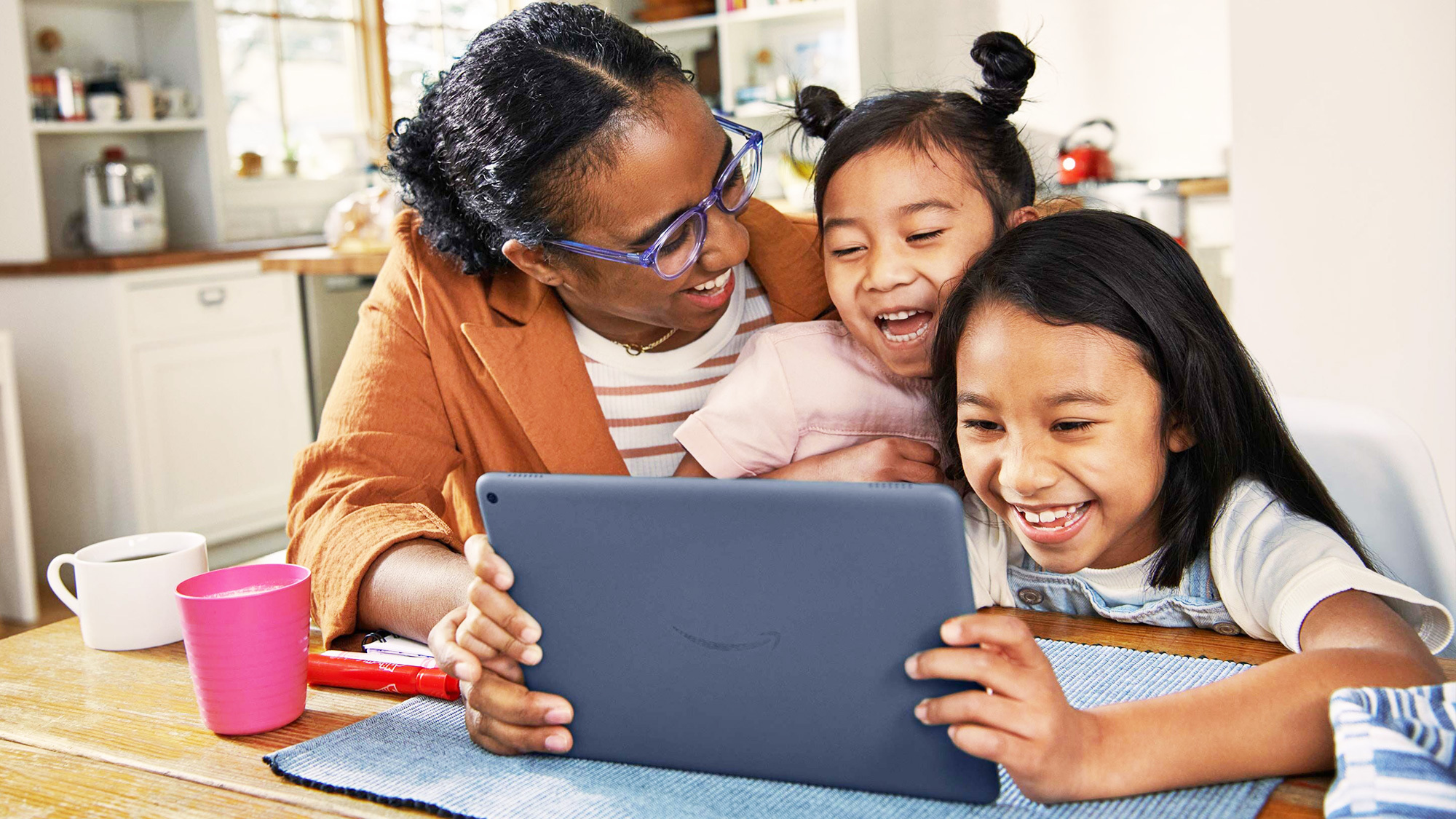 An image of a mother and two children smiling while looking at an Amazon device. 