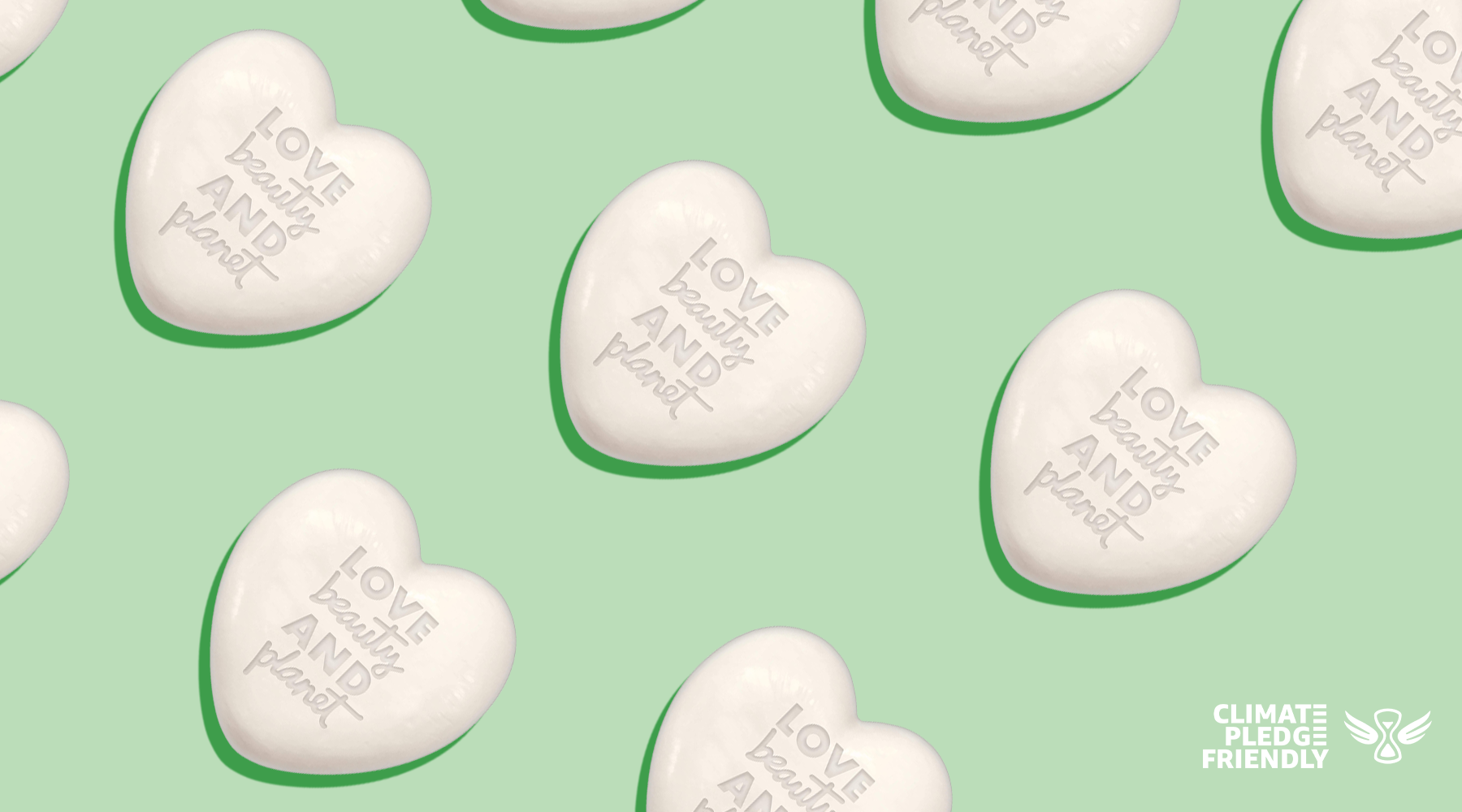 A light green color as the background with the Climate Pledge Friendly logo in white font placed in the bottom right corner. White solid 3D hearts that read "love beauty and planet" are placed diagonally across the image.