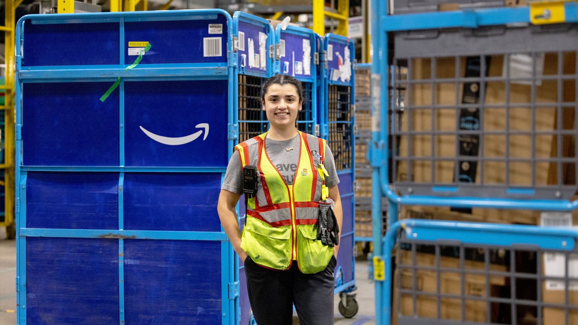 Amazon employee in safety vest smiling next to blue delivery carts