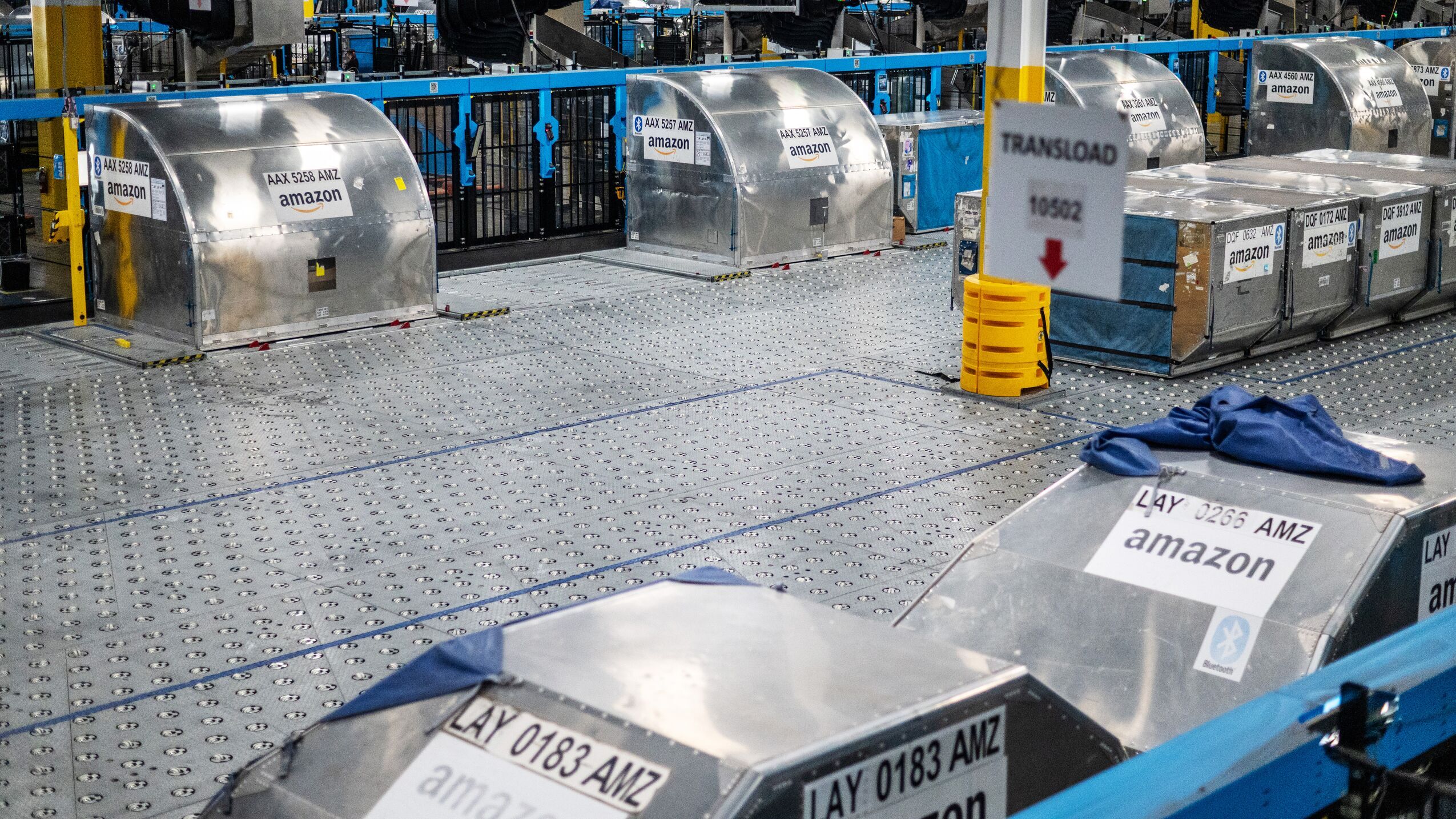 An image from inside an Amazon Air hub. The photo shows big, silver containers stationed on a metal platform. The platform has a series of wheels, locks, and bumps that guide the containers when they move. The containers each have big, white labels on them with the Amazon logo and various codes that denote what's in them.