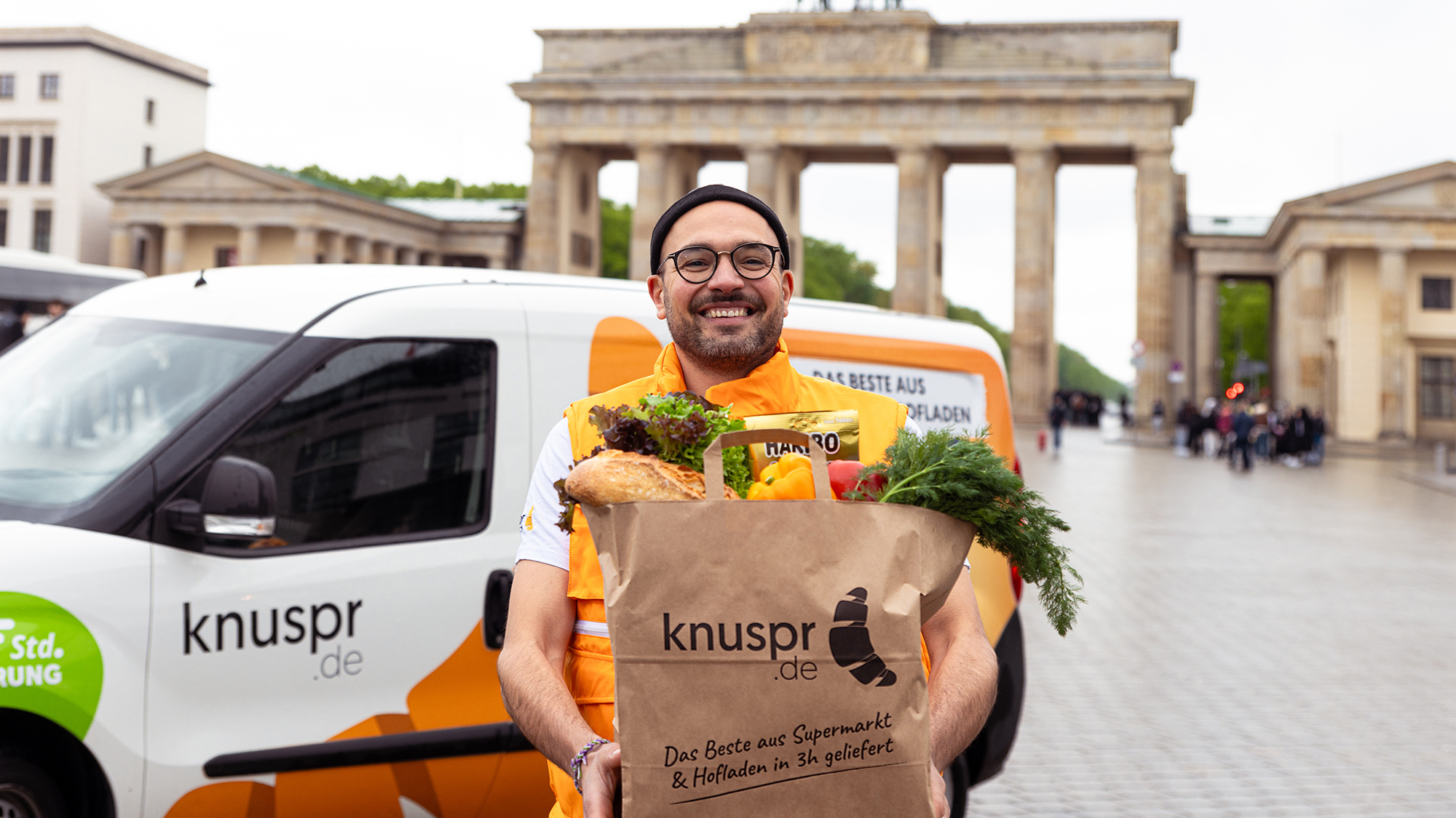 Ein Mann hält ein Tüte mit Lebensmittlen vor dem Brandenburger Tor. 