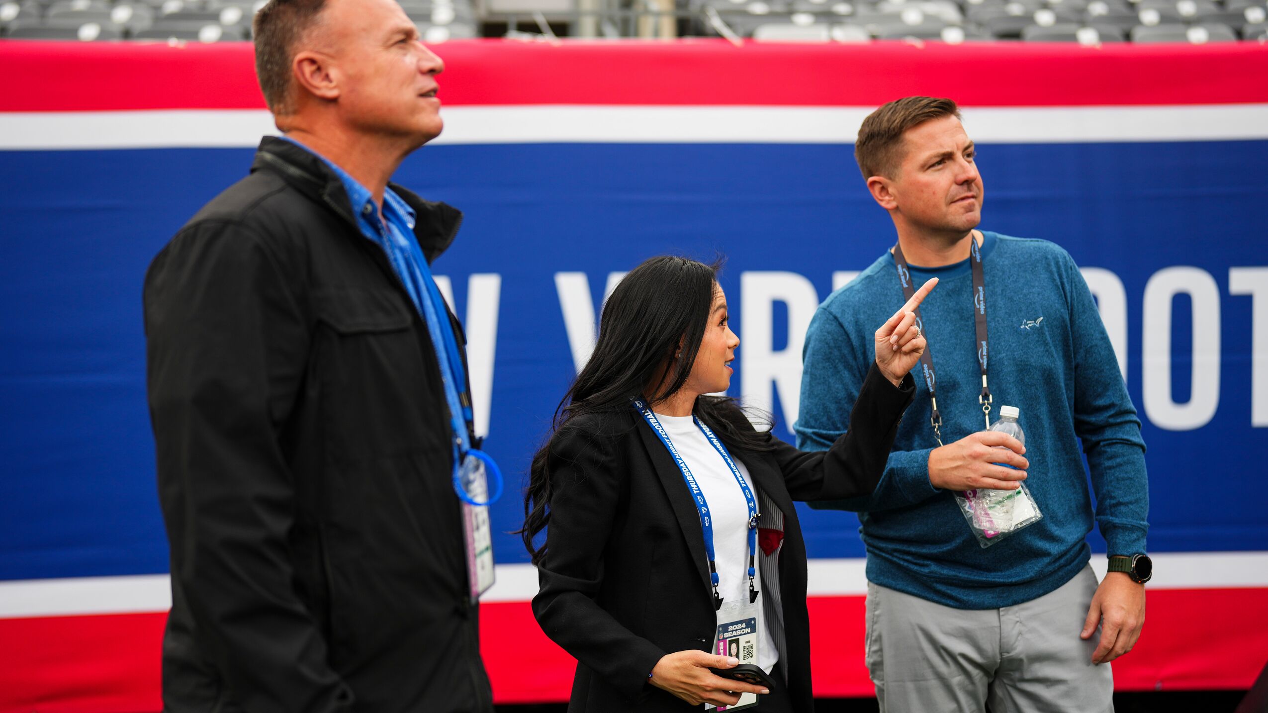 Two men stand with a woman who is pointing on a football field