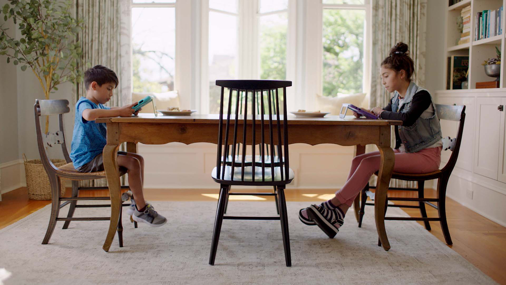 An image of two children at a kitchen table. Both are looking at tablet devices. 