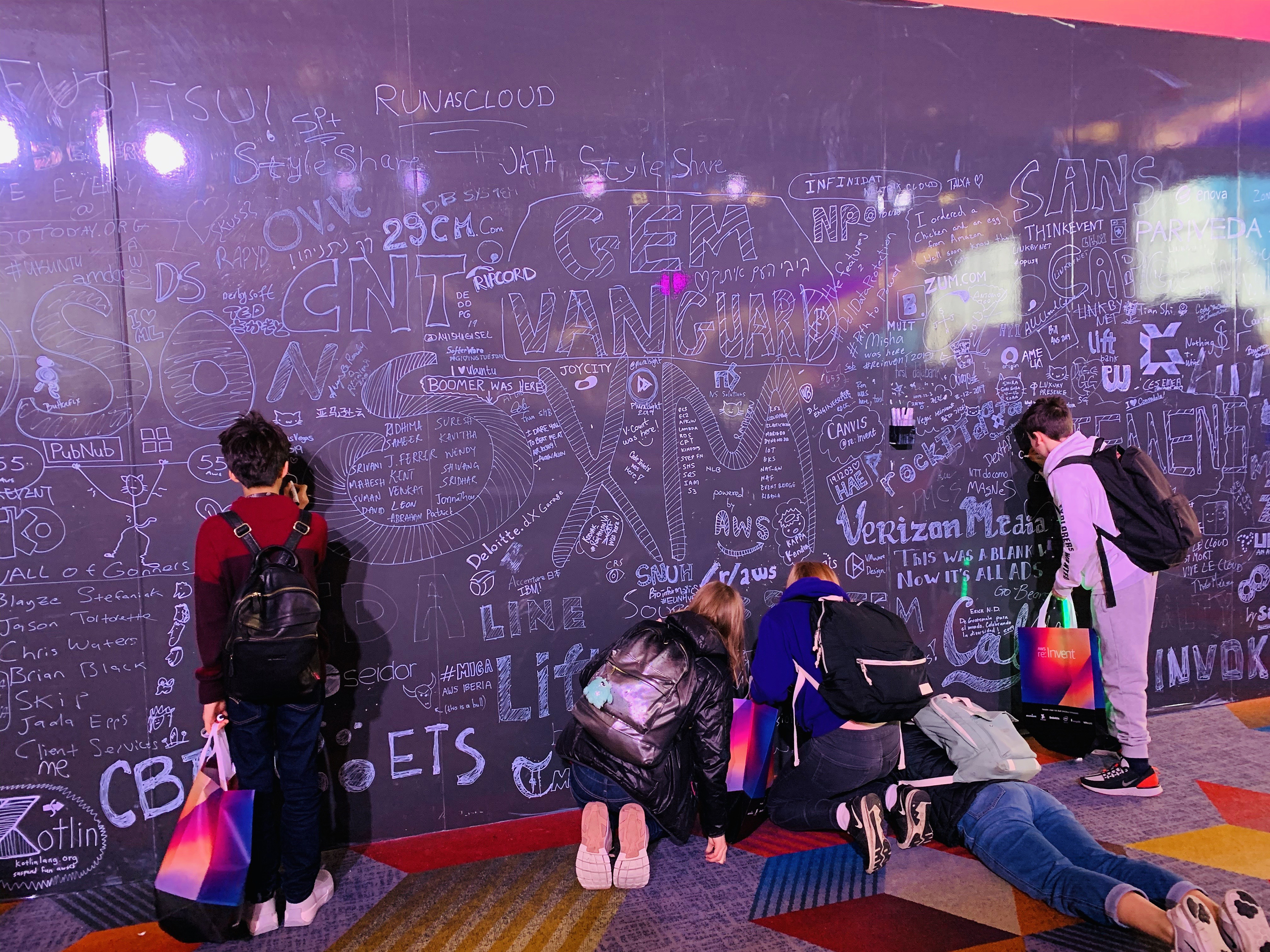 AWS GetIT students drawing on a giant blackboard which is filled with messages and doodles.