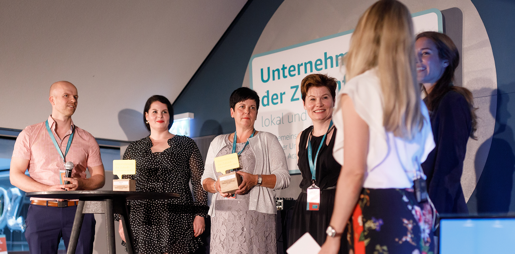 Die Gewinnerinnen von Unternehmerinnen der Zukunft stehen auf der Bühne und freuen sich über den Pokal. Im Hintergrund sieht man das UdZ Logo.