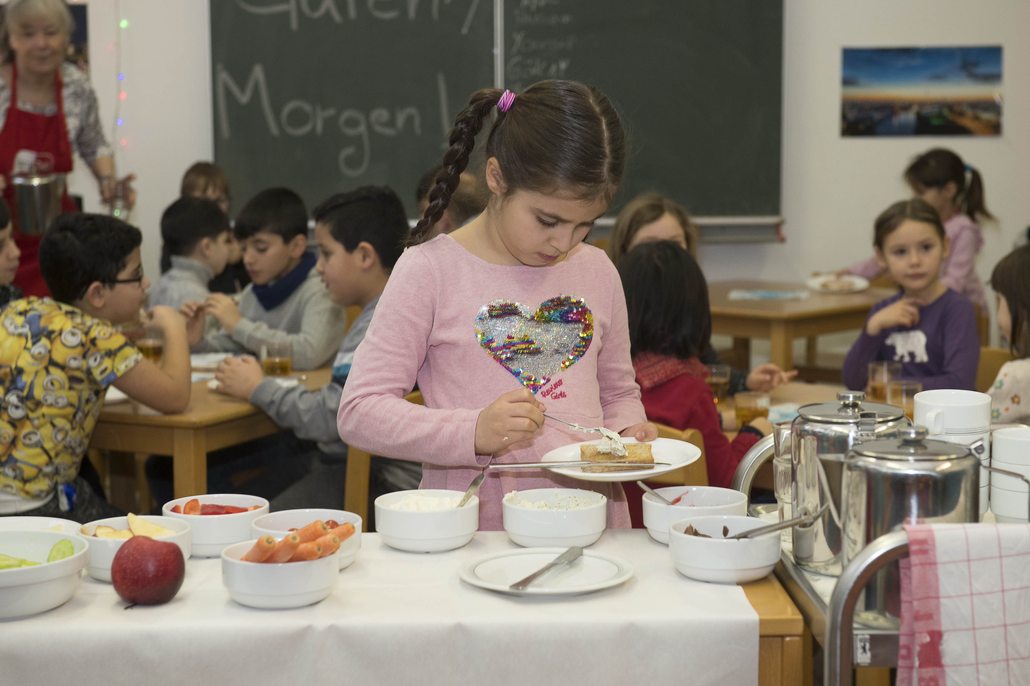 Ein kleines Mädchen in rosa T-Shirt steht an einem Frühstücksbuffet